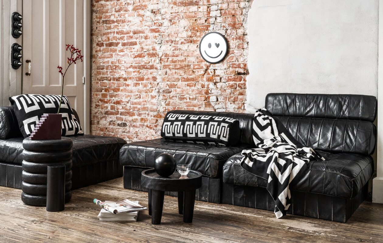 Zwart-wit rond kussen, gebreid bci-katoen, 20x50 cm € 49,95, zwart-witte plaid met verschillend dessin aan beide kanten, gebreid bci-katoen, 130x170 cm € 99,95, zwarte metalen vaas, 20x20 cm (Øxh) € 34,95. Overig privébezit. vtwonen 10-2023 | productie en styling Tanja Saarberg | fotografie Stan Koolen