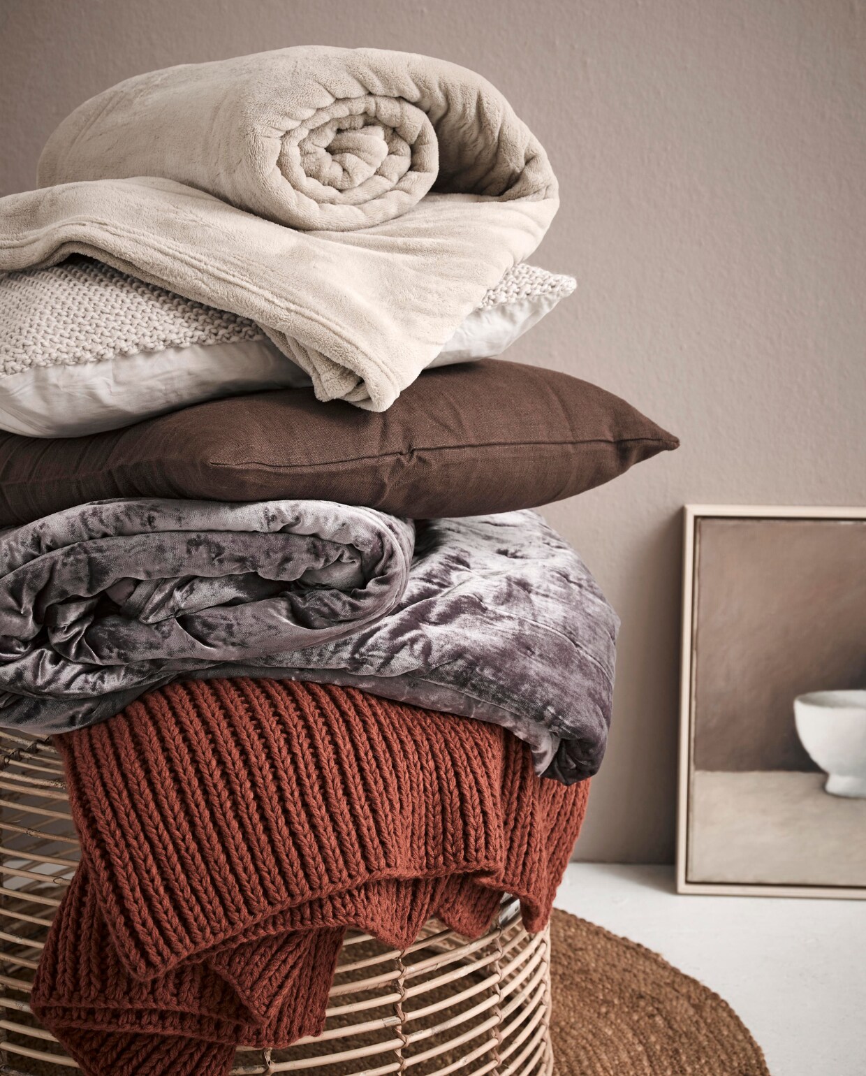Op de wand matte krijtverf in kleur Somerset Mauve per liter € 37,20 (Pure &amp; Original). Rond juten kleed € 25,-(Kwantum). Bijzettafel Rattan vanaf € 44,99 (Trendhopper). Terrakleurige plaid € 39,99, velours sprei 260x260 cm € 129,-, wollen grof gebreid écru kussen € 19,99 (H&amp;M Home). Bruin kussen € 7,99, sprei Trattviva 230x250 cm € 29,95 (Ikea). Kunst van SBK Kunstuitleen Amsterdam. vtwonen 05-2018 | styling Fietje Bruijn | fotografie Alexander van Berge