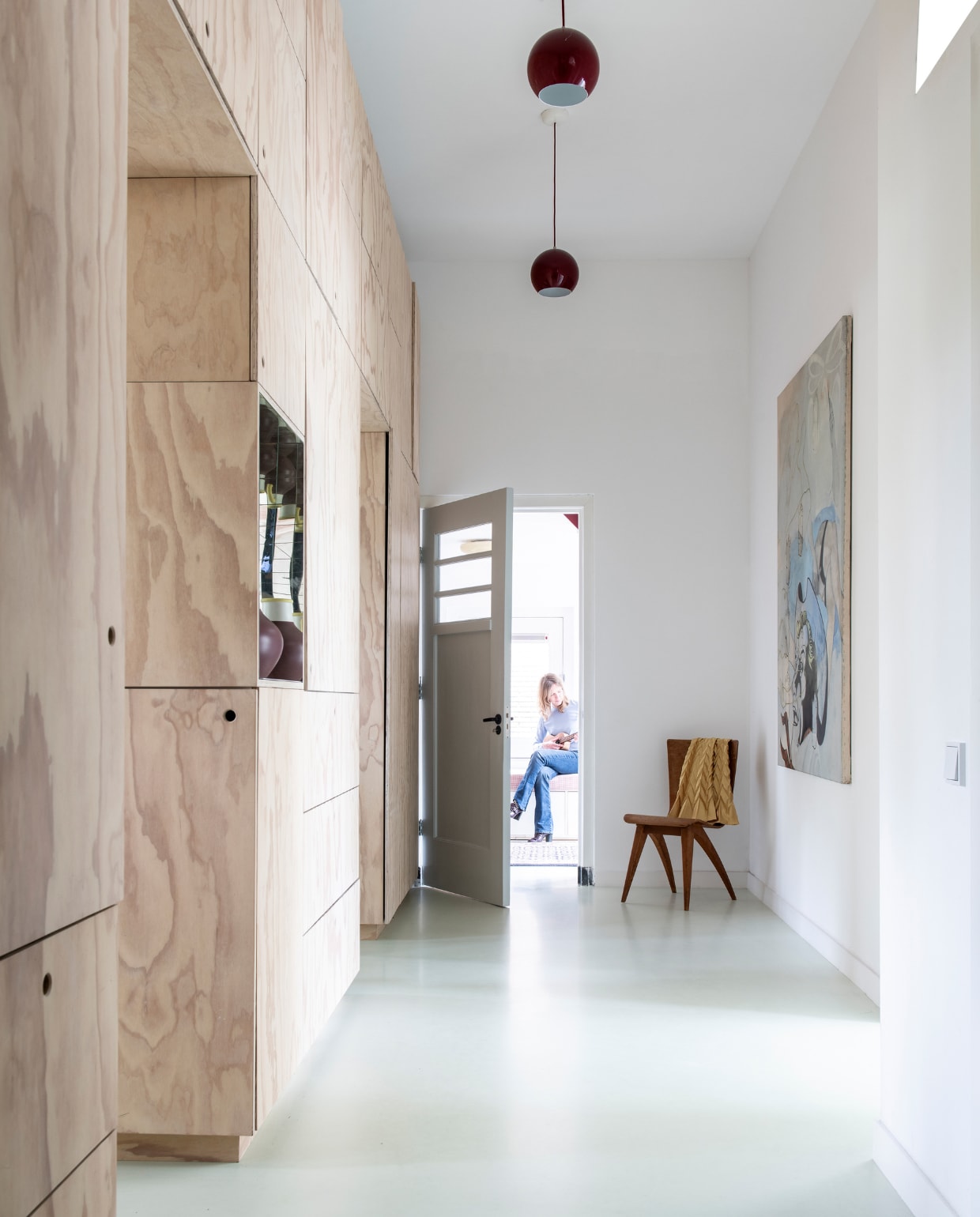 De entree van de oude school. De wandkast van underlayment is een ontwerp van Carmen van der Velde en gemaakt door vormgever/meubelmaker Mischa van der Wekke. In de kast een vaas van Ikea. Schilderij ‘Cowboy’ van Stella de Boo. Rode hanglampen Topan van Verner Panton. De stoel is een cadeau. Vloer ComfortFloor Pro van Sika in de kleur S1010/GY05.Wie Clementine van Wijngaarden (49, journalist), Luc (17) en Kate (15) vtwonen