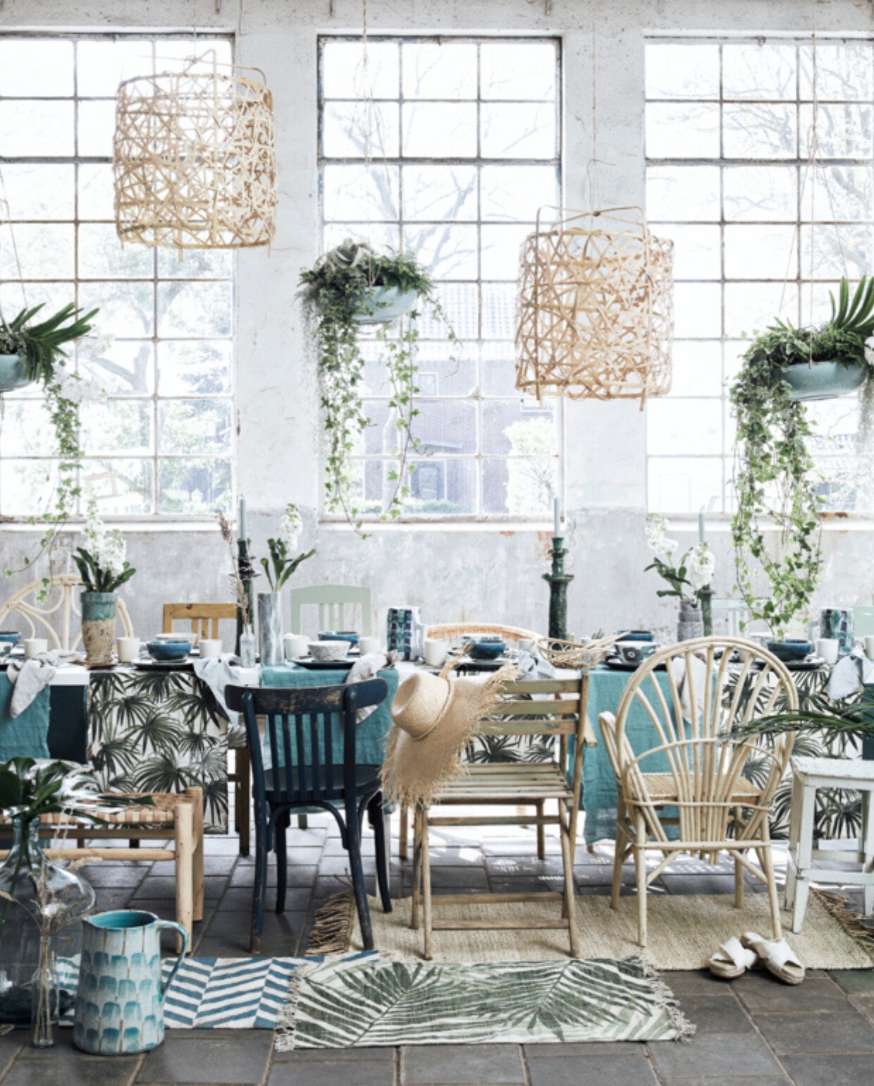 Witte tafel, lichtgroene klapstoel, kan op voorgrond, blauw-bruine vaas op tafel, lichtblauwe kan op bankje, hoge vaas rechts achter, alles prijs op aanvraag (com-anders.nl). Blank houten bankje met geweven leren zitting € 195,-, blank wilgenhouten stoel Essaouira met gebogen rug voor en achter de tafel per stuk € 139,-, kaarsenstandaards per stuk € 69,- (householdhardware.nl). Blauwe, groene en blank houten stoelen per stuk € 45,-, glazen vazen per stuk € 55,-, witte houten kruk € 25,- (vandijkenko.nl). Blank houten hanglampen per stuk € 455,-, beige rieten vloerkleed 80x150 cm € 122,-, blauwe kaarsen € 9,90 (letoile.store). Rieten stoel achter de tafel (alleen de bovenrand te zien) € 150,-, vloerkleden met print prijs op aanvraag, kunsttakken vanaf € 9,95, blauw-groen-witte kan van Serax € 45,50, groene krat prijs op aanvraag, schaaltjes met bloemdessin € 5,95, rieten flessenmand prijs op aanvraag, blauw-witte vaasjes van Serax op tafel € 47,95, vierkant groen kussen op bankje € 20,- (loods5.nl). Blauwe linnen stof als tafelloper, breedte 278 cm per meter € 82,- (wva.nl). Tafellopers met palmprint per stuk € 9,99, blauwe kommen € 7,99, blauwe borden € 9,99, groene plaid € 29,99, rond rotan dienblad € 24,99, witte mokken € 3,99, groene lepels per set van 3 € 9,99, witte slippers € 24,99, lantaarn van zeegras € 24,99, lichtblauw gewassen linnen servetten per stuk € 4,99, ronde blauwe pot met deksel in rotan dienblad € 12,99 (hm.com). Hangplanten met schalen en overige groendecoratie op maat, prijs op aanvraag (judithslagter.nl). Rieten hoed € 35,99, mand met witte driehoeken € 45,99 (zarahome.com). Beige linnen servetten Flax per stuk € 11,50 (bymolle.com). Overig privébezit. vtwonen 07-2019 | styling liza wassenaar | fotografie Alexander van Berge