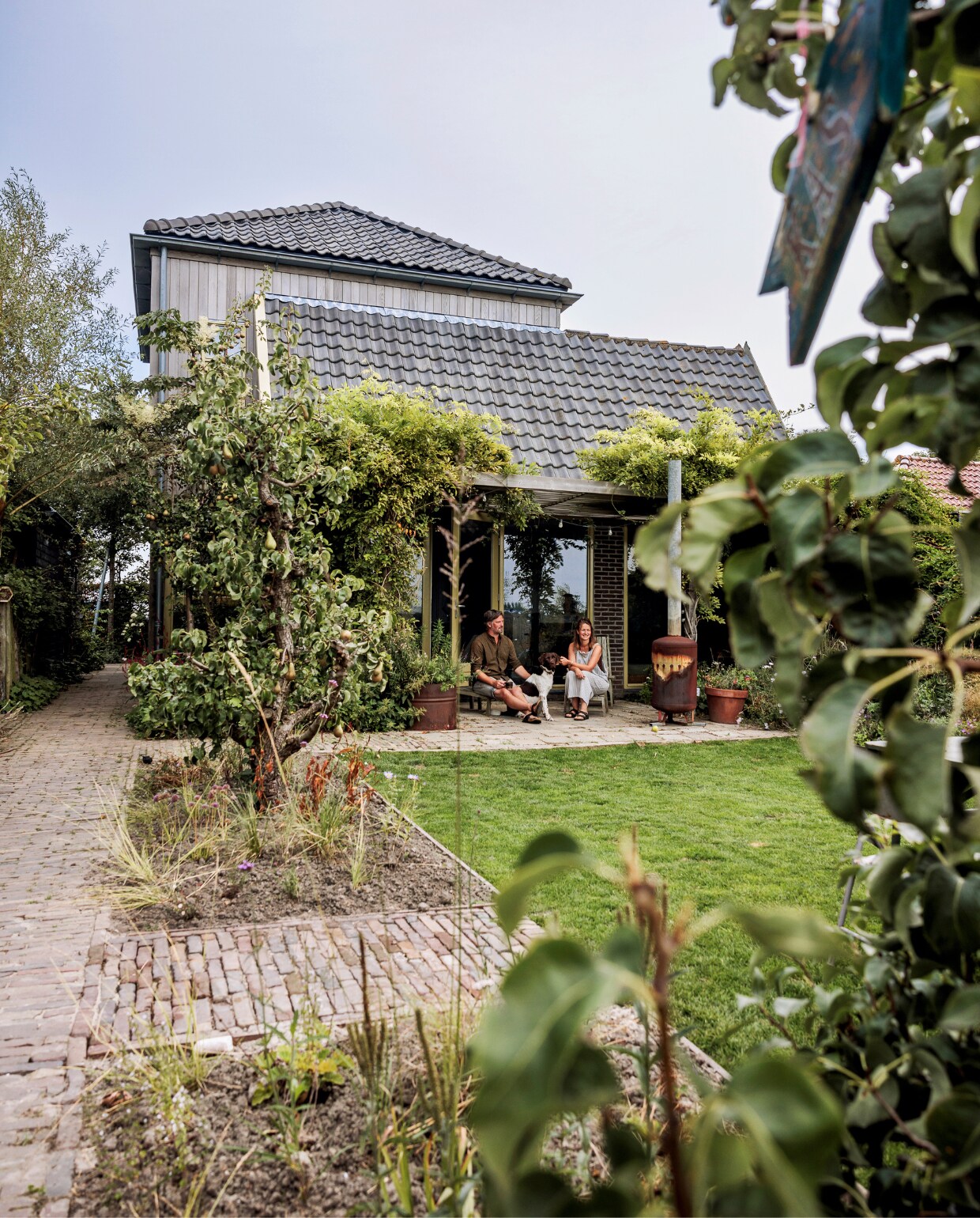 Terras met pergola aan de achterkant. Hier groeit blauweregen en clematis overheen. De borders links zijn in het voorjaar van 2023 aangeplant. Het hoge dak is de uitbreiding van het huis in de vorm van een kapberg. vtwonen tuinspecial 09 | styling Fietje Bruijn | fotografie Ernie Enkelaar