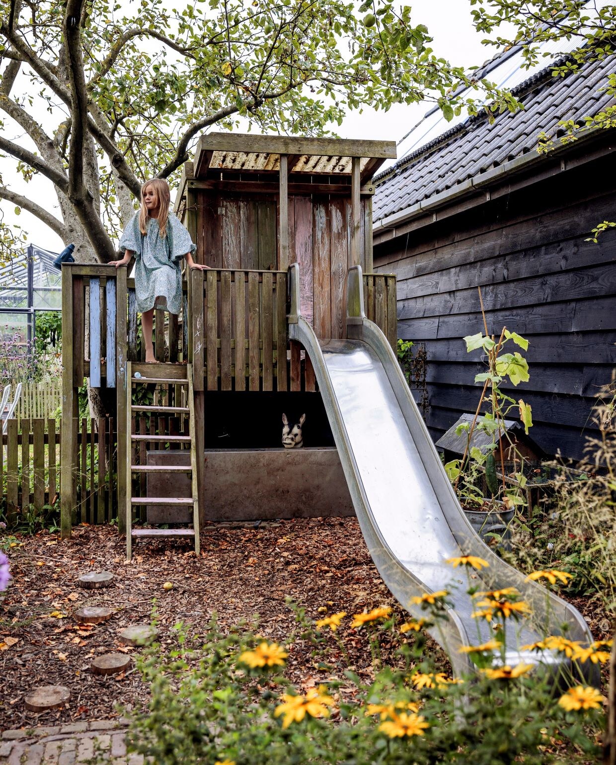De boomhut en de glijbaan vond Mark via Marktplaats. Mark bouwde de hut zelf weer op. Een klus waar zijn kinderen hem dankbaar voor zijn, want ze spelen dagelijks in de hut. De oude appelboom was als enige boom al aanwezig in de tuin. De gele bloemen op de voorgrond zijn zonnehoeden. vtwonen tuinspecial 09 | styling Fietje Bruijn | fotografie Ernie Enkelaar