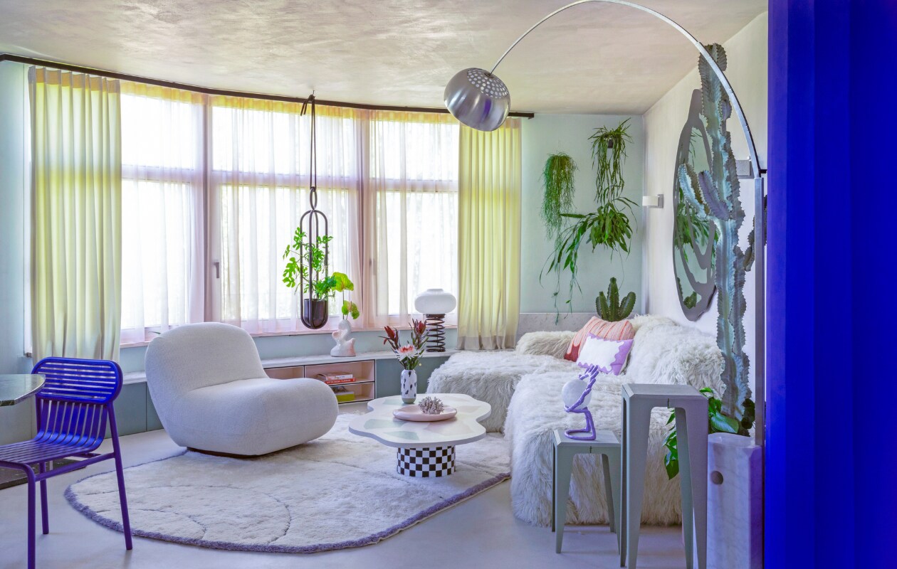 Gordijnen Ado Goldkante. Lage wandkast op maat gemaakt. Organische vaas Hannah Simpson Studio. Spiraallamp vintage. Plantenhanger Atelier Haussmann. Blauwe stoel Petite Friture. Fauteuil Chelsea BoConcept. Vloerkleed eigen ontwerp, handgemaakt in Marokko. Op maat gemaakte salontafel Minerva Artlab. Vaas Studio Arhoj. Roze bord Moustache. Bank Pyllow Mycs, schapenwollen bekleding zelfgemaakt. Bijzettafels Chamfer Wye Design. Paarse oog-lamp mattina moderna. Vloerlamp Arco Flos. vtwonen binnenkijken special 121-2022 | productie &amp; fotografie Anne Catherine Scoffoni