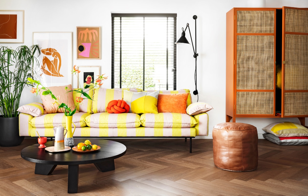 Driezitsbank Retro, 225x95x83 cm € 1925,-, oranje velvet kussen € 37,95, lijst rechtsboven Multi € 69,95, lijst daaronder Art Frame € 59,95, retro kast 125x40x200 cm (bxdxh) € 1495,-, koffiepot Seventies € 39,95, kopje op voet Kyoto € 3,75, dinerbord Peach € 19,95 (hkliving.nl). Kussen met grijze en gele vlakverdeling € 89,- (kus-sen.nl). Oudroze linnen kussen Empire € 45,-, leren poef Virginia € 159,95, salontafel Jay € 499,- (hetkabinet.nl). Sierkussen Knot van Design House Stockholm € 117,-, dienblad Imperfect van &amp;k Amsterdam (vtwonen.nl). Plantenpot Egg € 31,99 (praxis.nl). Plant Papyrus (Tuincentrum). Overig privébezit. vtwonen 08-2020 | styling Moniek Visser | fotografie Stan Koolen