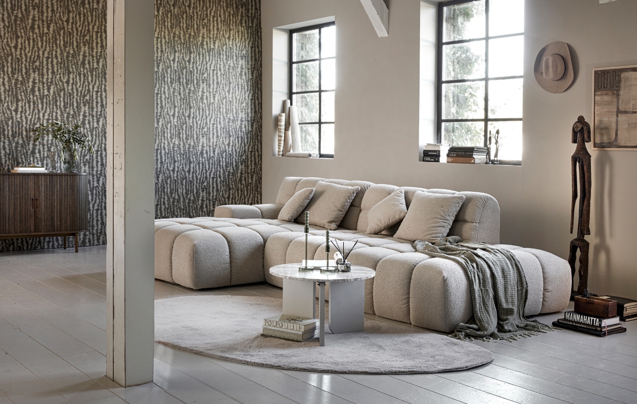 Loungebank Trentino, zelf samen te stellen, zoals afgebeeld 258x192x80 cm (bxdxh) € 1422,- (zitmaxx.nl). Vliesbehang Emerald Wild Ikat in 333443 van Eijffinger, 0,52x10 m (bxh) € 94,95 (eijffinger.com). Eikenfineer dressoir Lyngvig met 2 roldeuren, 120x40x80 cm (bxdxh) € 399,-, katoenen plaid Karve € 17,50 (jysk.nl). Geurstokjes € 15,99, eikenhouten lijst 30x40 cm € 15,99 (hm.com). Boeken € 5,-, houten tribalfiguren € 6,95, groot tribalbeeld € 40,- (rataplan.nl). Glazen vazen Grove, 12x22 cm (Øxh) € 9,- en 18x32 cm (Øxh) € 16,50, polyester vloerkleed Wallace € 90,-, marmerlook mdf bijzettafel Brez € 75,-, glazen kandelaars Avie, vanaf € 5,50 (kwantum.nl). Groene kaarsen € 5,50 (hema.nl). Kunstwerk zelfgemaakt. Overig privébezit. vtwonen 01-2024 | styling Marit Saladini | fotografie Peggy Janssen
