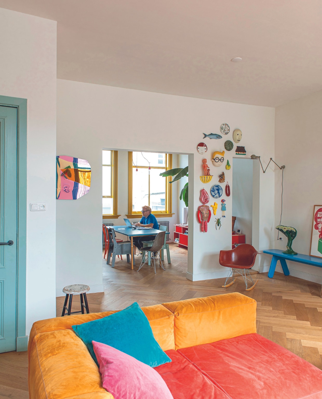 Blauwe bank Pow van Frank de Bruijn, oranje-rode bank Hay, biologisch model van een blad Catawiki, vintage lamp Jieldé, schommelstoel Eames, kruk rommelmarkt, spiegel Mo Man Tai. Aan de wand hangen onder andere: kunstwerk lichaam Nathalie Lété, sprinkhaan Intertoys, 3D-geprint pistool Foppe, hondenkop van een gevallen hondenbeeld. Gele plank, citroenen in net Mickey Philips. Masker Hay, kool uit winkel Piet Hein Eek en wat rommelmarktvondsten en cadeaus. Eettafel Muller Van Severen, oranje stoel Thonet, grijze stoel Piet Hein Eek, kuipstoelen Vitra, blauwe stoel Ikea, rood dressoir Tylko, vloer eiken visgraatparket. vtwonen 04-2023 | productie De Binnenkijkers | styling Jeske Weel | fotografie Caroline Coehorst