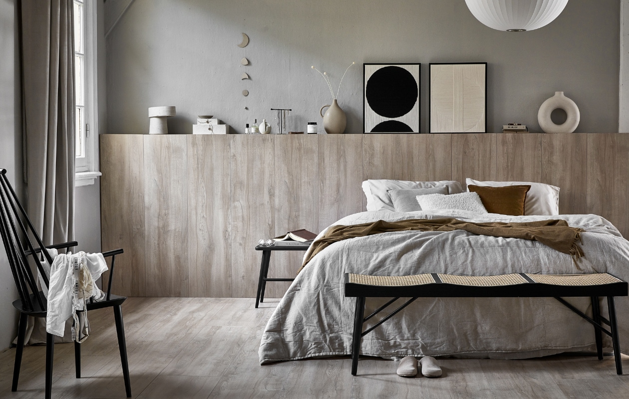 vtwonen collectie (Laminaat XL Board, kleur vergrijsd, per m² 23,99 (inhoud per pak 2,25 m², 5 lamellen per pak, afmeting lamel 138x32,6 cm (lxb), 8 mm dik, met groef)). M.m.v. karwei.nl (gordijn op maat van vtwonen in stof Cosy kleur 1166, muurverf Soft Grey van vtwonen), zarahome.nl (dekbedovertrek, kussens, plaid, zwarte houten bank met rotan, zwarte houten kruk, beige vaas met oor, geurkaars, sloffen), hm.com (witte ronde vaas), studio-yen.com (kunstwerk cirkels), vtwonen.nl (zwarte spijlenstoel van Hay, hanglamp van Hay), ohmyhome.nl (kleihanger), suhka.nl (beige doosje en wierook- houder). Overig privébezit. vtwonen 01-2021 | productie Tanja Saarberg | styling Kim van Rossenberg | fotografie Peggy Janssen