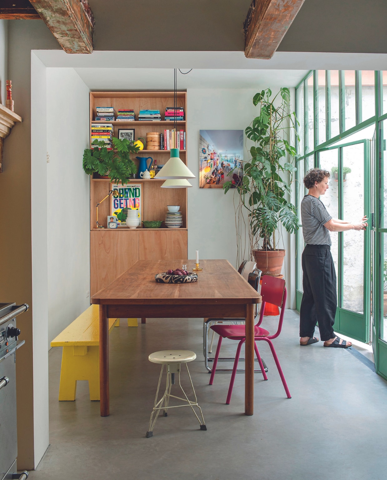Kast en gele bank gemaakt door Job. Stalen pui Metalworks, hanglampen Hübsch, vergadertafel tweedehands, buisstoel Gispen, foto van vorige huis bewoners door Thijs Wolzak voor NRC, voer gepolijst beton met vloerverwarming. Overig onbekend. vtwonen 04-2024 | productie De Binnenkijkers | styling Jeske Weel | fotografie Caroline Coehorst