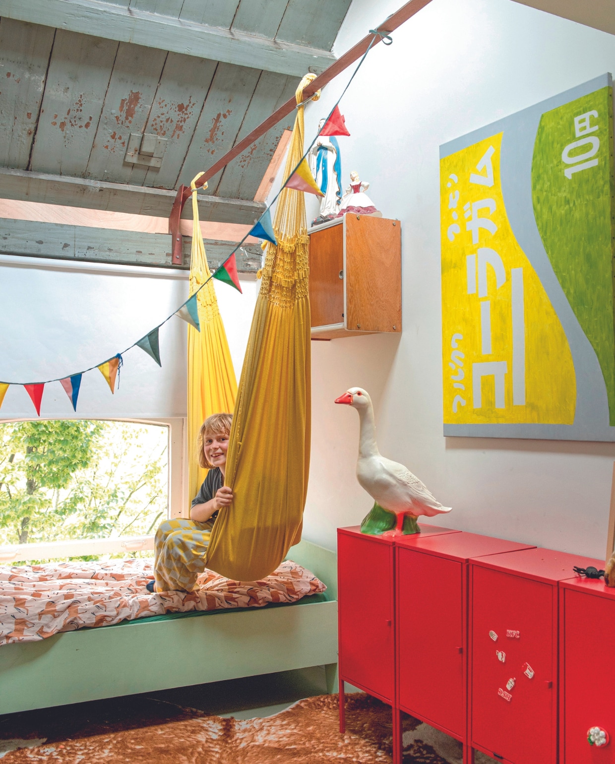 Hangmat cadeau, bed zelfgemaakt,dekbedovertrek Hema. Hangkast en Mariabeelden rommelmarkt. Rode kast en koeienhuid Ikea. Kunstwerk van Job, rolgordijn Praxis, slinger Engel. Overig onbekend. vtwonen 04-2024 | productie De Binnenkijkers | styling Jeske Weel | fotografie Caroline Coehorst