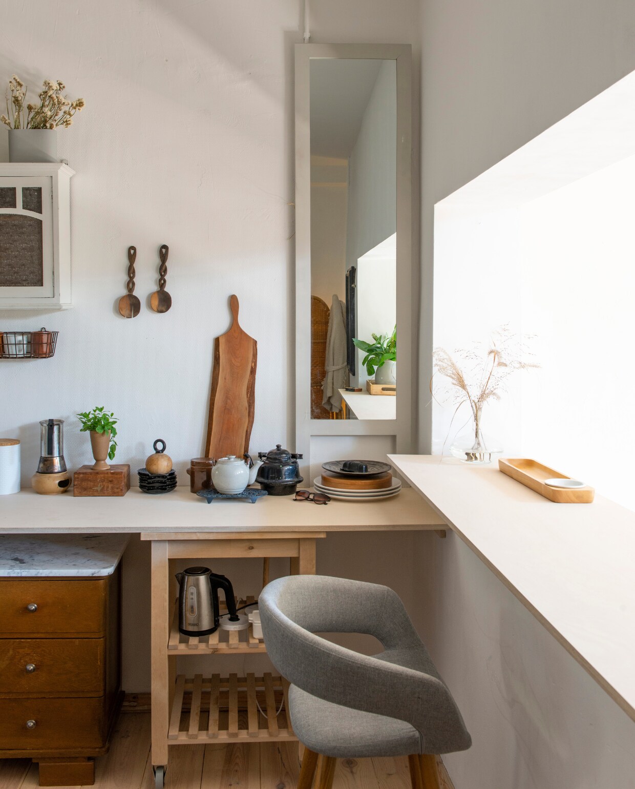 Witte voorraadbussen en zelf grijsgeverfde spiegel Xenos. Houten bar en verlengd keukenblad Woodchuck, lichtbruine lap Home by Door, droogbloemen Dreamlink via wish.com, barstoel Westwing Now, wit vaasje Edelman. Lamp vintage, samengesteld uit twee lampen, overig tweedehands van onder andere Rataplan. Herkomst vloer en sisal kleed onbekend. vtwonen 08-2021 | productie de binnenkijkers | styling jeske weel | fotografie caroline coehorst