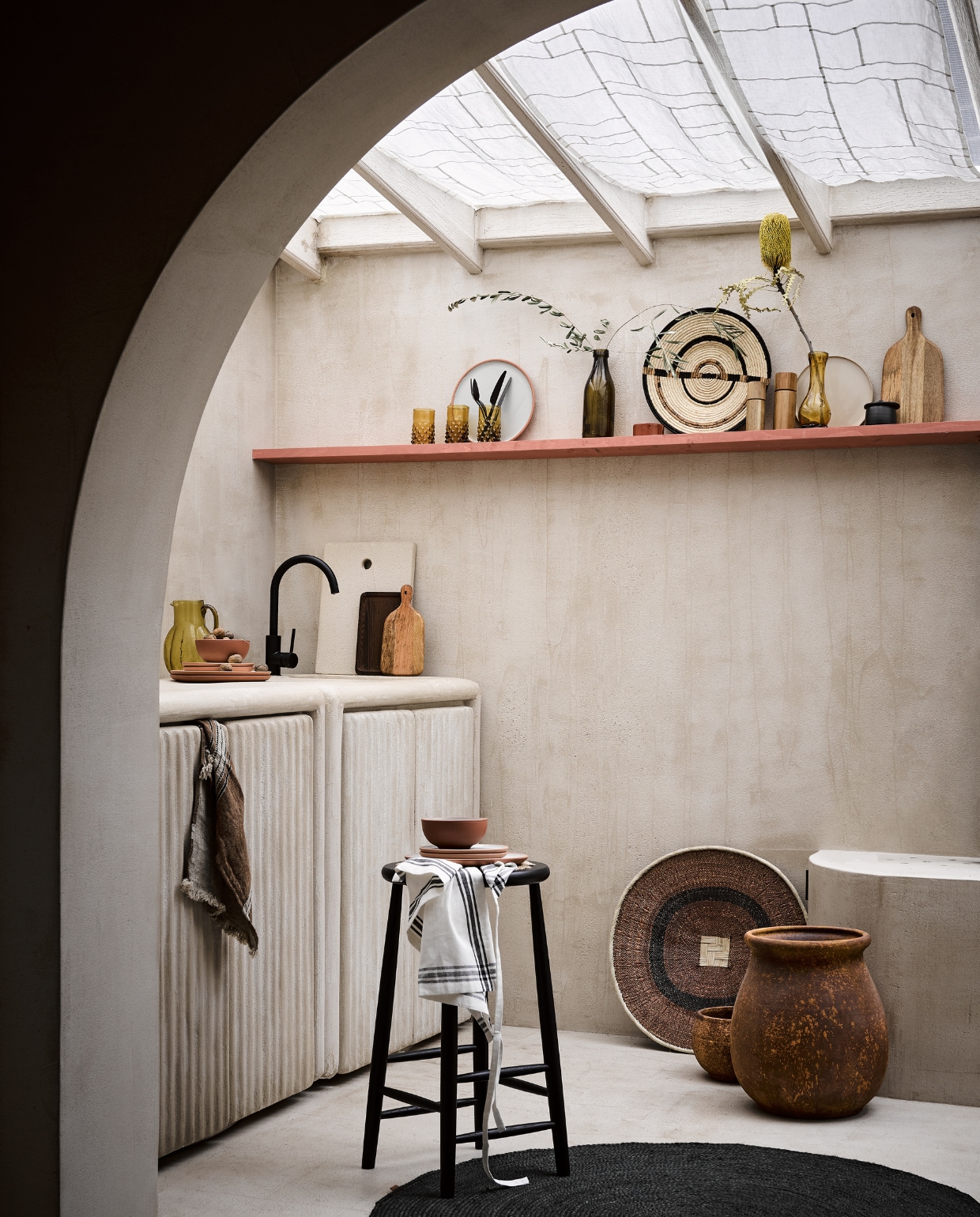 Linnen gordijnsheets gemaakt met pojagi techniek, prijs op aanvraag (bymolle.com). Plank geverfd in lakverf kleur Book Room Red No. 50 van Farrow &amp; Ball, per 2,5 liter € 97,- (deruamsterdam.nl). Zwart bestek Stella van Blomus op plank, 16-delige set € 129,99, acaciahouten peper- of zoutmolen van AdHoc, 17 cm (h) € 29,99, 14 cm (h) € 24,95, beige bord Terres de Reves in Misty Grey van Serax, 22 cm (Ø) € 18,40, dienblad Heii van Serax, 25x16 cm € 26,95, zwart rond vloerkleed Eternal van Ferm Living, 120x120 cm € 94,50 (vtwonen.nl). Microcement stuc op wand en vloer, prijs op aanvraag, inbouwkeuken met kraan per unit, vanaf € 2000,-, gestuukt dienblad tegen achterwand € 75,-, grote bruine vaas op de grond € 149,95, kleine bruine pot € 62,50, terra servies met groene binnenkant, schaaltje € 11,95, ontbijtbord € 14,95, groot bord € 16,95, klein terra schaaltje op plank € 14,95 (lanena-home.com). Houten snijplank groot € 12,99, klein € 9,99, wit schort met zwarte streep € 7,99 (hm.com). Droogbloemen (plantje.nl). Amberkleurig glas op plank met tak, per stuk € 13,-, mosterdkleurige fles met olijftak € 39,-, mosterd-kleurige glazen vaas met sierlijke vorm € 99,-, zwarte suikerpot € 47,-, mand met witte rand op grond, 58 cm (Ø) € 59,-, geweven mandschaal small op plank € 73,-, groene karaf op keukenblok art deco € 63,-, donkerbruine theedoek met streep van Libeco € 27,- (couleurlocale.eu). Zwarte kruk met rotan bovenkant J165B van Møblér € 689,- (homestede.nl). vtwonen special 03-2022 | styling Liza Wassenaar | fotografie Alexander van Berge | assistentie Demelza Krens | locatie lanena-home.com