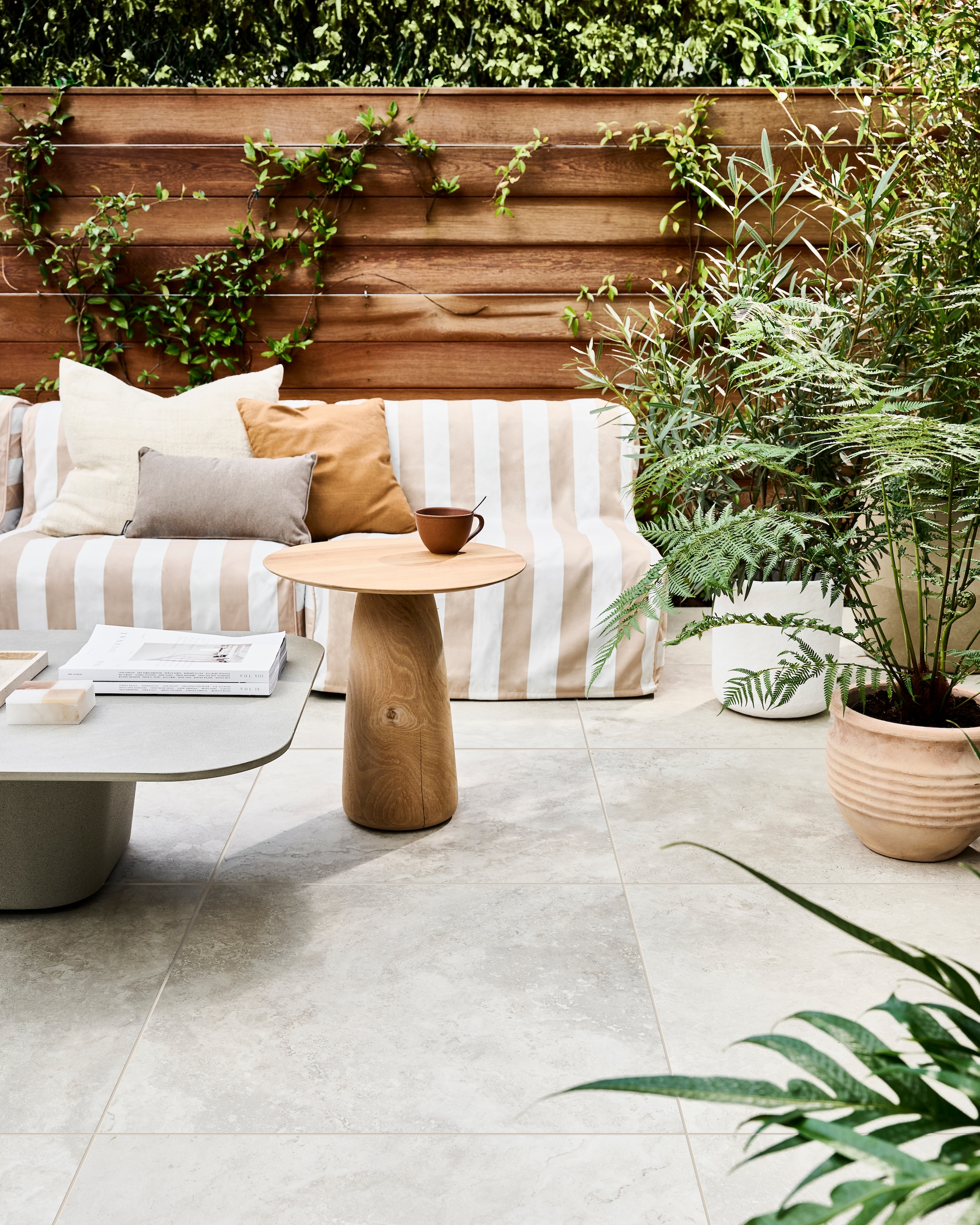 Tuintegel Solostone Uni Dust Off  White, 70x70 cm, per m² € 74,50.M.m.v. basiclabel.nl (opblaasbare fauteuils Sit on Air van vtwonen), dacks.nl (salontafel, bijzettafel), intratuin.nl (terracotta bloempotten, groot bruin kussen, klein bruin kussen), vtwonen.nl/shop (witte bloempot van Serax), zarahome.com (travertin plateau). Overig privébezit. vtwonen 05-2024 Huiscollectie tuintegels | styling Marlies Does | fotografie Sjoerd Eickmans
