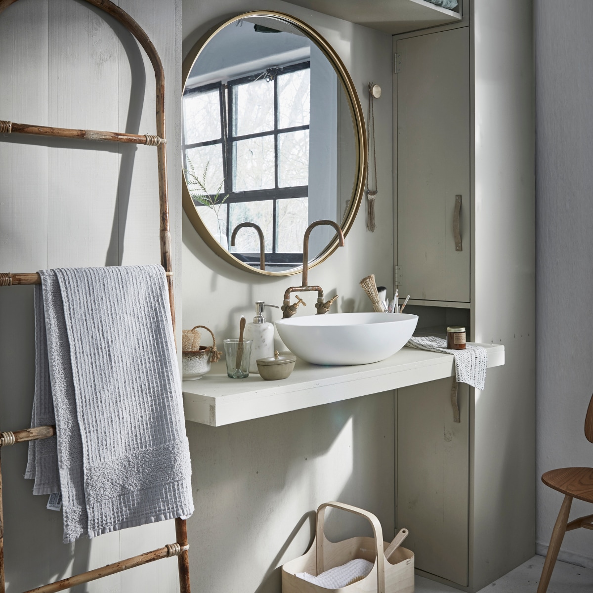Grote ronde spiegel Ø 80 cm € 249,-, marmeren zeeppomp € 41,- (Nordal). Bamboe ladder € 54,05, vloerkleed 60x90 cm € 23,65 (Madam Stoltz). Witte wafeldoek € 49,95 (De Weldaad). Stoel Butterfly van Ercol € 625,- (De Machine- kamer). Berkenplex opbergmand 25x40x36 cm € 89,50 (Nordic New). Grijze handdoek 90x150 cm € 35,99(Zara Home). Waskom Girona, 57x40x15 cm € 381,- (Ton Scholten). Kraan € 75,- (Jan van IJken Oude Bouwmaterialen). Tadelakt zandkleurig potje met deksel € 19,95 (MaisonNL). Bureaulamp € 95,-(Vint. Amersfoort). Glas € 3,95, linnen doek in opbergzak € 75,-, witte opgerolde wafeldoek € 45,- (De Weldaad). Zandkleurig met bruine kom € 39,99, messing muurknop van Ferm Living € 20,-, geurkaars in bruin glazen potje € 16,- (Six and Sons). Rieten mand in kast vanaf € 9,99 (H&amp;M Home). Badborstel € 8,95 (Dille &amp; Kamille). De kast is geschilderd in de kleur Bone van Farrow &amp; Ball per 0,75 liter € 44,- (De Ru). De muur is geschilderd in de kleuren Egg White en Light Grey van vtwonen, per liter € 18,95, per 2,5 liter € 32,95 (Karwei). vtwonen 05-2018 | styling Cleo Scheulderman | fotografie Jeroen van der Spek
