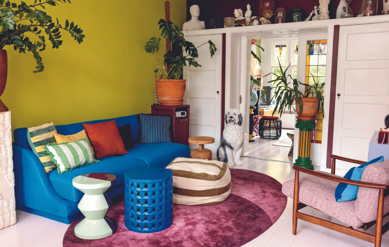 Verfkleur groen Acid Green van Farrow &amp; Ball. Witte zuil, groen-oranje zuil Marktplaats. Vaas kringloopwinkel, bank Sofacompany, vierkant gestreept kussen HKliving, rechthoekig gestreept kussen Sissy-Boy, blauw gestreept kussen Palais. Overige kussens, tweekleurige bijzettafel Carice van Houten, vloerkleed en stoel Polspotten. Poef en blauwe bijzettafel Loods 5. Houten bijzettafel Hans van Bentem. Hond en bloempotten tuincentrum. Kussen twee kleuren blauw Byborre, lavendelkleurige kast Mustard Made, windlicht rommelmarkt, beamerkast zelfgemaakt, knijplamp Merci, rotan poef vintage, borstbeeld gemaakt door Sharvin. Overige accessoires kringloopwinkel, erfstukken en rommelmarkt. vtwonen 04-2024 | styling Ilona Jongepier | fotografie Dana van Leeuwen