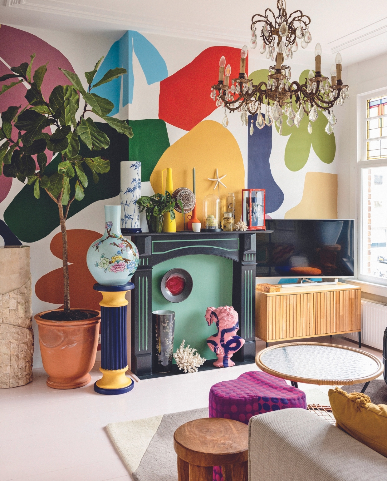 Marmeren zuil en zelf geschilderde pilaar Marktplaats. Terracottapot tuincentrum. Gebloemde vaas, gele vaas, oranje kandelaar, poef en houten bijzettafel Polspotten. Lamp vintage. Vitrinekast, donkere vaas, koraal en bijzettafel met glazen blad kringloopwinkel. Blauwe vaas gemaakt door Sharvin, tv-meubel Woood, bord Norman Trapman, plant Marvy Green. Overig onbekend. vtwonen 04-2024 | styling Ilona Jongepier | fotografie Dana van Leeuwen