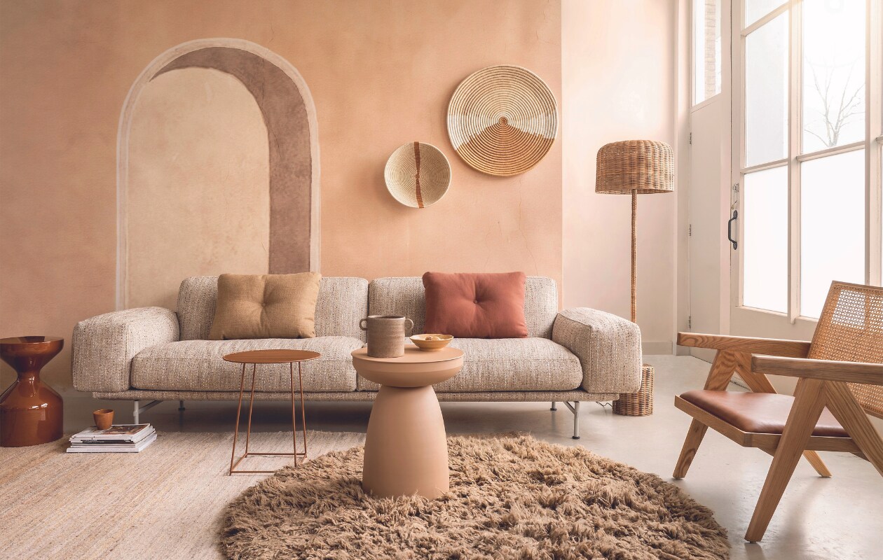 Behang Alcove in Oyster, 3 panelen, prijs op aanvraag (masureel.com). Duurzame bank Prime in stof Salone, ontwerp door Studio Truly Truly, 275x91x78 cm (bxdxh) € 6410,- (gelderlanddesign.com). Vloerkleed Fluffy van HKliving, wol en katoen, 150 cm (Ø) € 675,-, kom Kyoto van HKliving, set van 4 € 39,95 (vtwonen.nl/shop). Juten vloerkleed Nessa van Linie Design in Naturel, 170x240 cm € 580,-, fauteuil La Roche van Loods 5 in Naturel, hout, leer en rotan, 70x66x78 cm (bxdxh) € 395,-, metalen bijzettafel Archie van Loods 5 in Salmon, 40x50,5 cm (Øxh) € 99,95, metalen bijzettafel Flippo van Serax, 40x46 cm (Øxh) € 154,- (loods5.nl). Metalen bijzettafel Floyd in Tapenade, 30x47 cm (Øxh) € 99,- (hetkabinet.nl). Rotan vloerlamp Cane € 750,-, terracotta koffiekop Juniper € 25,- (nordal.com). Rieten manden aan de muur, handgevlochten € 189,- en € 89,- (maisonsuku.com). Kussens Dot, katoen, linnen en polyester, per stuk € 89,- (hay.nl). Overig privébezit. vtwonen 05-2024 | styling Marianne Luning | fotografie Stan Koolen | assistentie Julia Beitler &amp; Rosa Neuteboom