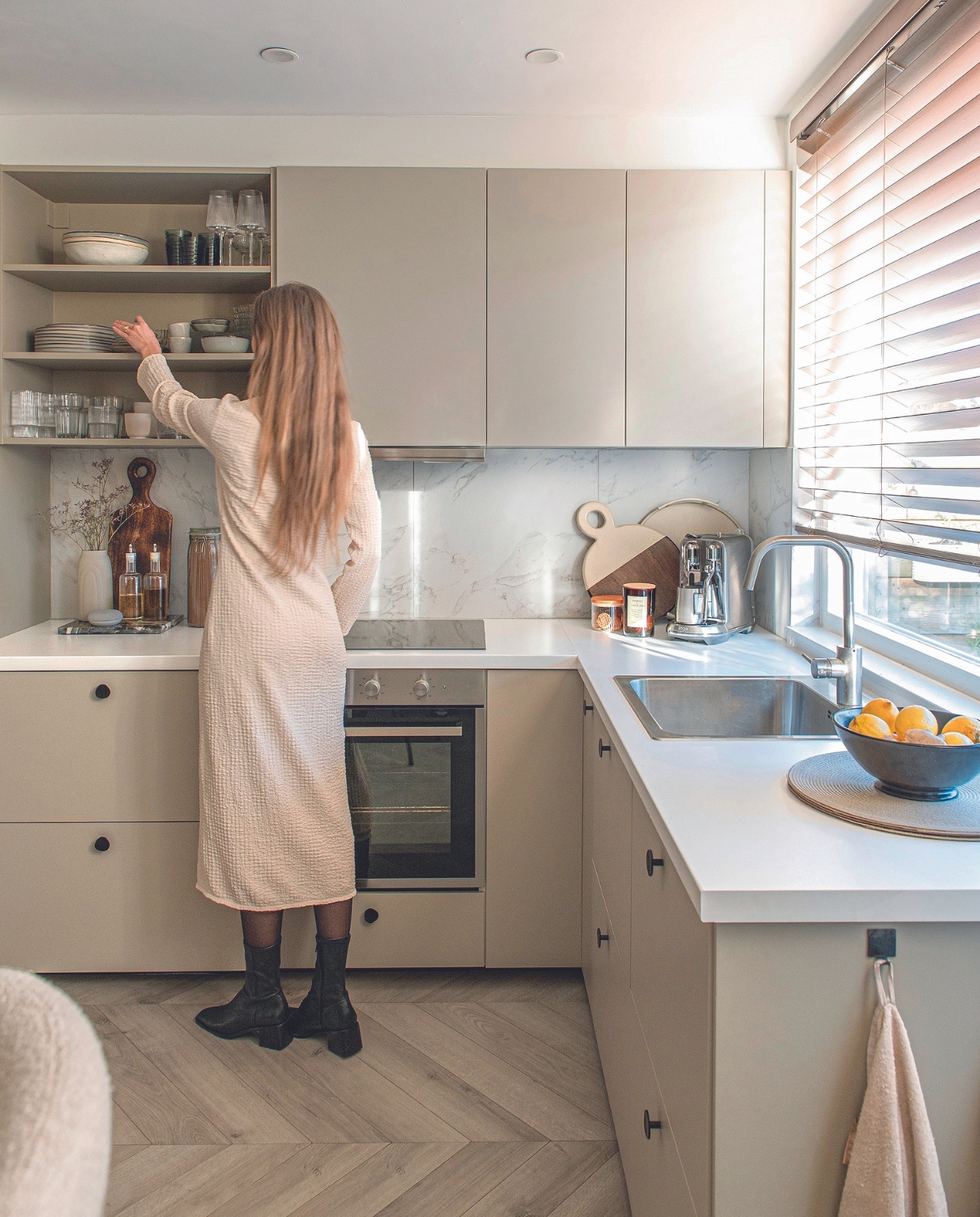 Kastfronten Havstorp van Ikea in beige, zijpanelen geverfd in NCS S 3005-Y20R, meubelknoppen Zara Home, jaloezieën Veneta. Rechthoekige serveerplank en handdoek Blokker. Vaas en fruitschaal kringloop. Speaker Google Nest. Koektrommel en olie- en azijnset Hema. Weckpot Ikea, ronde serveerplank Gusta, dienblad Light &amp; Living geverfd in NCS S 3005-Y20R, koffiemachine Nespresso Creatista. Geurkaars en placemats H&amp;M Home. Servies in open kast van boven naar beneden en van links naar rechts: schalen Casa, glazen Iittala, wijnglazen blokker. Borden Ikea, gestapelde gebaksborden kringloop en Søstrene Grene, mokken Casa, schaal Ikea. Glazen Blokker, glazen Ikea, mokken Nespresso, organische glazen Kwantum, mokken Casa. Overig onbekend vtwonen 04-2024 | productie De Binnenkijkers | fotografie Caroline Coehorst | styling Jeske Weel