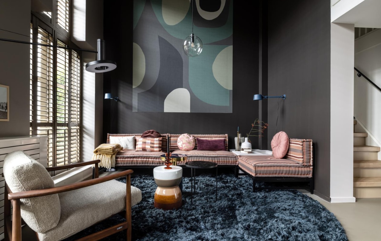 Lange wand met shutters in kleur Boomschorsbruin, Flexa. Donkere hoek waar bank staat in kleur Fading Horizon, Flexa. Op maat gemaakte shutters in de kleur rustic grey, JASNO shutters. Op de wand behang mural Artifact – 312483, Eijffinger. Elementenhoekbank, Householdhardware. Kussens, Householdhardware. Fauteuil Todd van Pols Potten, Eijerkamp. Vloerkleed Arezzo op maat gemaakt, Eijerkamp. Blauwe bijzettafel Glam, Zuiver. Zwarte bijzettafel Glazed, Zuiver. Keramische kruk Glazed, vtwonen. Intuitive waxinelichthouder Arabian Spice van Urban Nature Culture, vtwonen. Wandlampen Bolt wall sidefit, thunder blue (bij bank), Tonone. Wandlamp Beads wall 120 (bij fauteuil), Tonone. Hanglamp glazen bol Warsaw, Itsaboutromi. Antique brass kaarsenstandaard van BePureHome, basiclabel. Papier mache vaas van BePureHome, basiclabel. Witte vaas, privébezit. Plaid Ice cream, basiclabel. Wit kussen Escapism van Urban Nature Culture, vtwonen. Ruiten kussen Midtown van Urban Nature Culture, vtwonen. Rond kussen met goud, vtwonen. Paarsachtig kussen, vtwonen. Roze rond kussen, vtwonen. vtwonen Weer verliefd op je huis seizoen 15, aflevering 9 | styling Fietje Bruijn | fotografie Sonja Velda