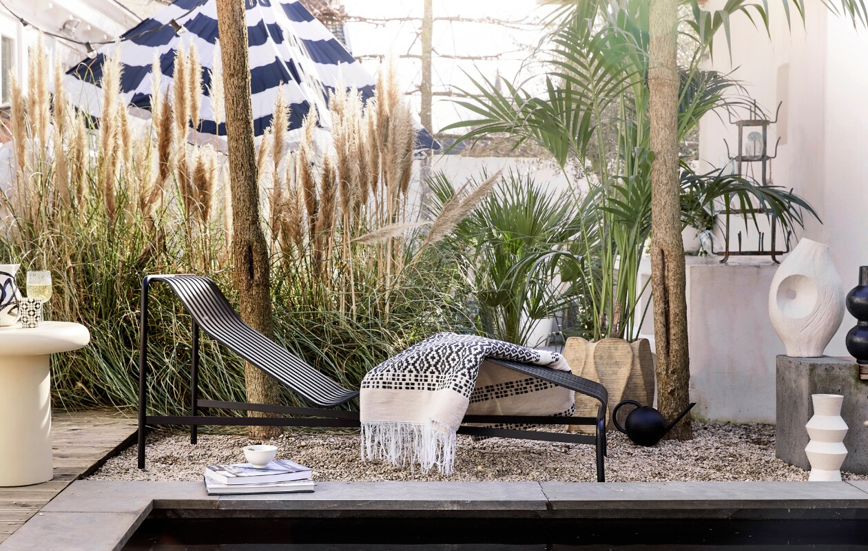 Antraciet daybed Palissade van Hay, gepoedercoat staal, 164,5x65,5x70 cm (lxbxh) € 999,-, zwart-witte waxinelichthouder € 4,95 (loods5.nl). Parasol Stripesol, 350 cm (Ø) € 479,- (fatboy.com). Wollen plaid € 172,50, polyester bijzettafel, 50x50 cm (Øxh) € 359,-, zwarte tadelakt vaas Bubbles € 119,-(householdhardware.nl). Gerecycled wijnglas € 19,50 (serax.com). Zwart-witte kan van Bachmara € 29,90 (ateliersem.nl). Plantenpot met ribbels € 195,-, vaas met gat € 91,95 (ptmd.nl). Witte kom Kyoto € 6,-, witte vaas met zigzag-reliëf € 38,- (hkliving.com). Vintage flessenrek € 89,- (cininwonen.nl). Gieter privébezit. vtwonen 06-2023 | styling Kim Timmerman | fotografie Peggy Janssen