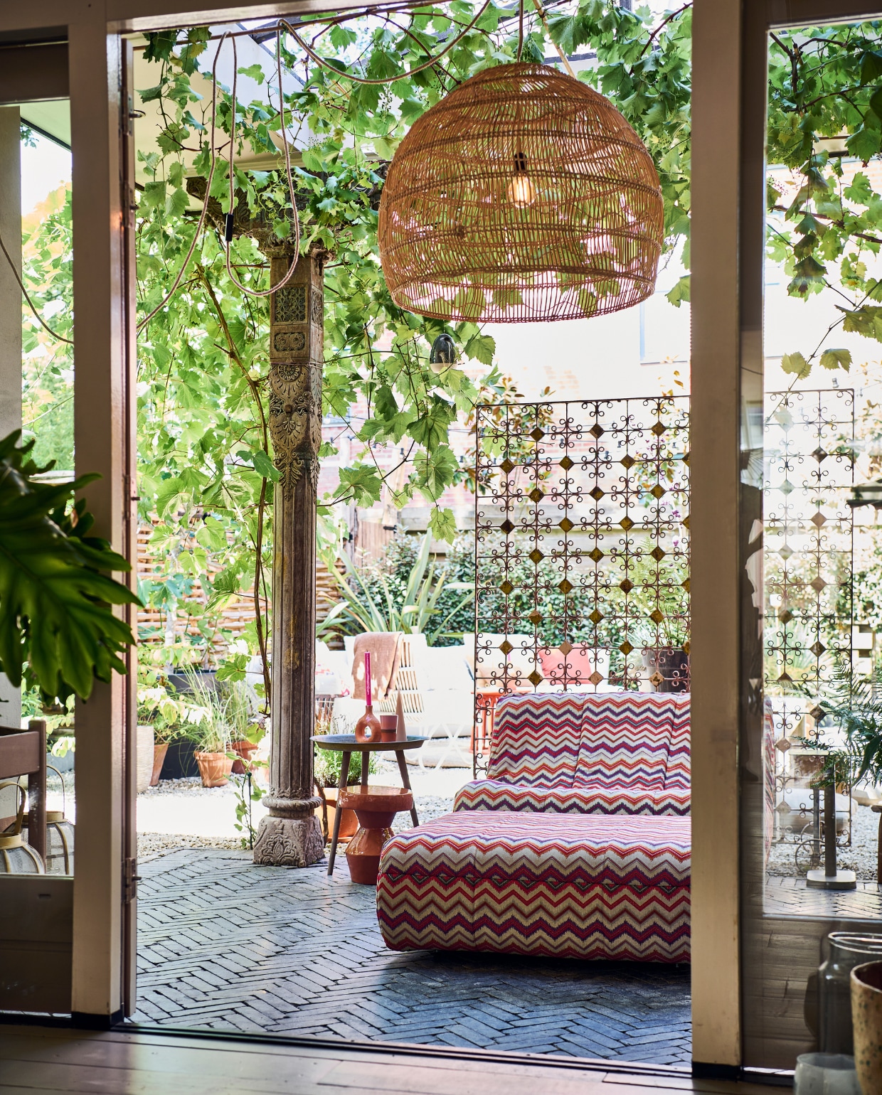 Outdoor loungebank met hocker Muna met stof Fiesta van evavandeven.nl. Keramieken bijzettafel Urban Nature Culture, bijzettafel op poten Kwantum, kegelkaars H&amp;M Home, kandelaar Household Hardware. Hanglamp en mok HKliving. Pilaren stonden er al. Op de vloer klinkers van Belgisch hardsteen. vtwonen tuinspecial 10 | styling Liza wassenaar | fotografie Sjoerd Eickmans