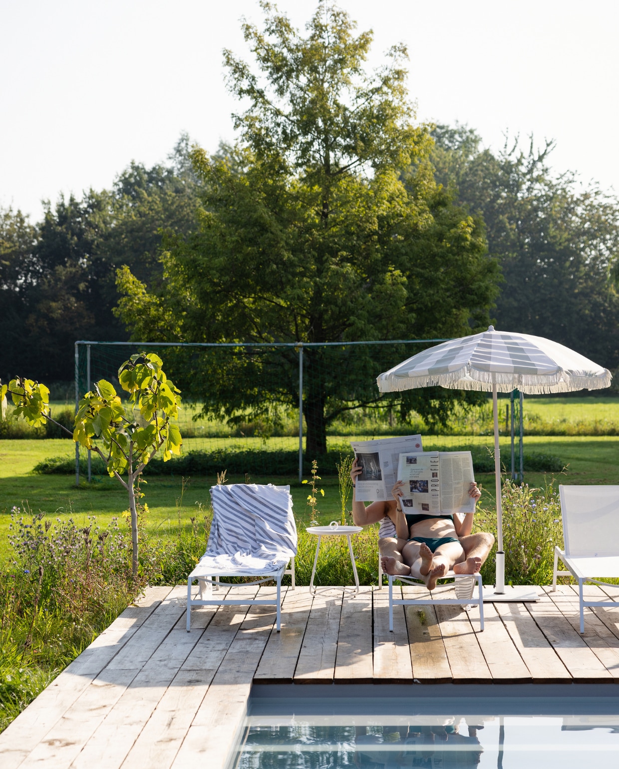 Links een vijgenboom, langs de vlonders een strook ingezaaide wilde bloemen, op de achtergrond een voetbalgoal voor zoon Tijs die keeper is. Ligstoelen Maisons du Monde, parasol Kwantum, tafel Spijck. vtwonen Tuin 10 | styling Ilona Jongepier | fotografie Dana van Leeuwen