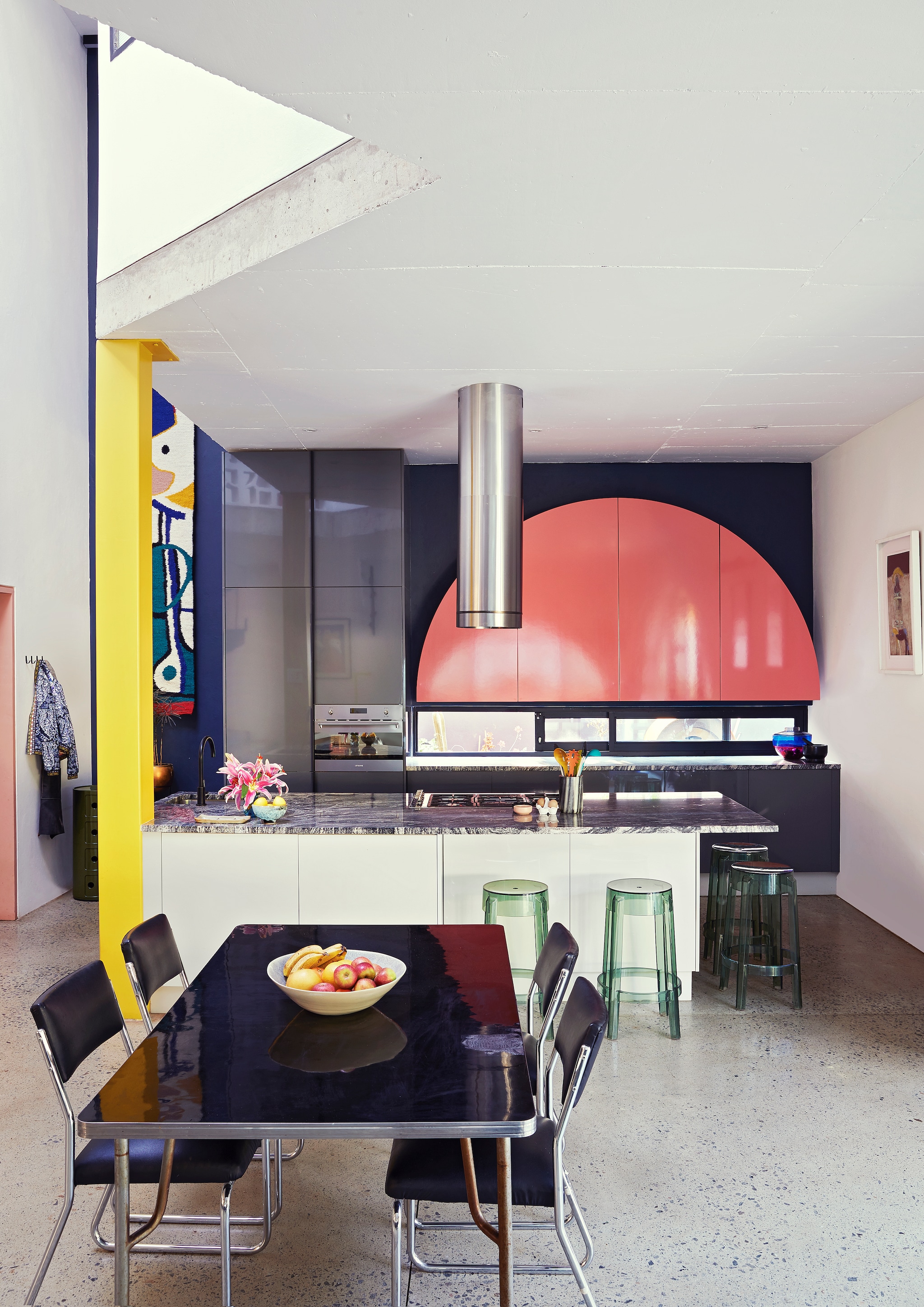 Keuken ontworpen door Gregory Katz via ProReno Kitchens, met werkblad van Namibisch graniet International Slate Sales. Vloer gepolijst beton World of Decorative Concrete. Groene bijzettafel Componibili, barkrukken Charles Ghost en blauw-roze vaas Shibuya Kartell. Eettafel en chromen buisstoelen vintage. Fruitschaal Wonki Ware. Zwarte haken Leroy Merlin. Wandkleed Renée Rossouw. vtwonen special binnenkijken 06-2021 | productie Living Inside, Bureaux | fotografie Elsa Young