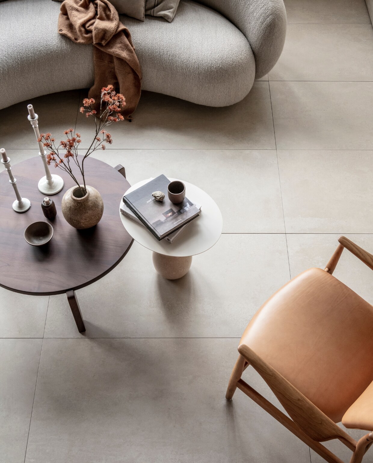 Op de vloer: vloertegel Raw in kleur Sand, 60x120 cm, per m² € 69,-. M.m.v. justhaasnoot.nl (staande lamp, bank Julep van Tacchini, salontafel Guéridon Bas van van Vitra, witte bijzettafel Lato van &amp;Tradition, fauteuil van hout met leer van House of Finn), zarahome.com (witte metalen kandelaars, stenen vaas), suhka.nl (textielkunstwerk, kom en mok). Overig privébezit. vtwonen 11-2021 | productie Tanja Saarberg | styling Kim van Rossenberg | fotografie Sjoerd Eickmans