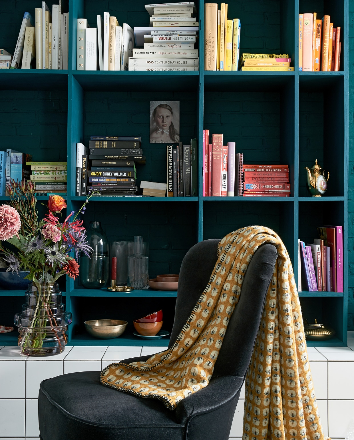 Boekenkast in kleur Marina Blue matte lak € 45,- per liter (Little Green). Fluwelen stoeltje Remsta € 149,- (ikea.nl). Plaid Klara € 79,- (made.com). Rood kommetje € 2,99, mat gouden theepot € 9,99 (xenos.nl). Grijze glazen vaas Ruby grey € 19,99 (casashops.com). Geribbelde vaas Hilmir € 12,99, vaas Manfred € 9,99 (jysk.nl). Kunstbloemen v.a. € 2,95 (casashops.com). Foto vrouw, prijs op aanvraag (racheldubbe.com). Overig privébezit. vtwonen 03-2020 | styling Fietje