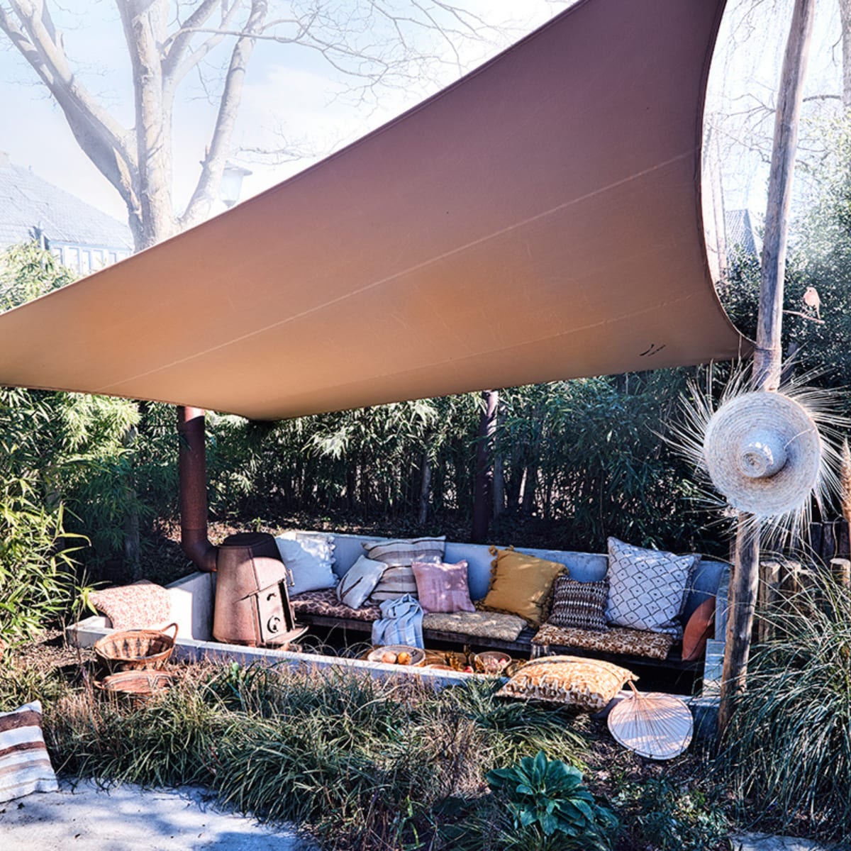 Tent schaduwdoek op maat gemaakt (tentworx.nl). Hoed, gestreept berber kussen 50×50 cm, ecru kelim kussen met pijl 50×50 cm, groot berber kussen met schuine ruit 80×80 cm, groot gestreept kussen 75×75 cm, roze kelim kussen 50×50 cm, decoratief waaier, bamboe salontafel van Tine K Home 70x150x45cm (bxlxh), manden in het gras, naturel linnen handdoek van Libeco (couleurlocale.eu). Gedessineerde matraskussens 60×100 cm, grote kussens met kwasten 65×65 cm, kussen met oranje batik dessin 50×50 cm, kussen met bordeauxrood en oranje dessin 50×50 cm, allemaal Madam Stoltz (deens.nl). Ronde rattan draaistoel Peacock van Arti 89x81x73 cm (lxdxh) (fonteyn.nl). vtwonen TUIN 02-2020 | styling Cleo Scheulderman | fotografie Jeroen van der Spek