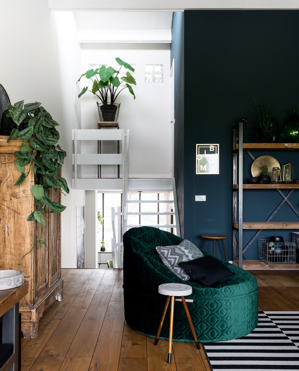 De stellingskast is gemaakt door een meubelmaker. Groene poef www.studiomust.nl. Kussens in poef: zwart kussen gemaakt door een vriendin, grijs kussen via www.viacannella.nl. Kist onder tafel, bijzettafeltje rond beton en vintage kruk naast kast Marktplaats. Groene vazen en metalen bakken in de kast kringloop. Gouden vitrinekastjes Hema. Popjes in vitrinekastje Lammers &amp; Lammers. Zwarte kleine vaasjes www.helladuijs.nl. Rubberen bloempotje www.bleqshop.nl. Lamp in kast Zuiver. Draadmand in kast www.heterfgoed.com. Vaas in mand Ikea. Huislampje op kast House Doctor. Muurkleur Deep Ocean extra mat Histor. Eikenhouten vloer Cisco vloeren Venray. vtwonen 09-2017 | fotografie Stan Koolen