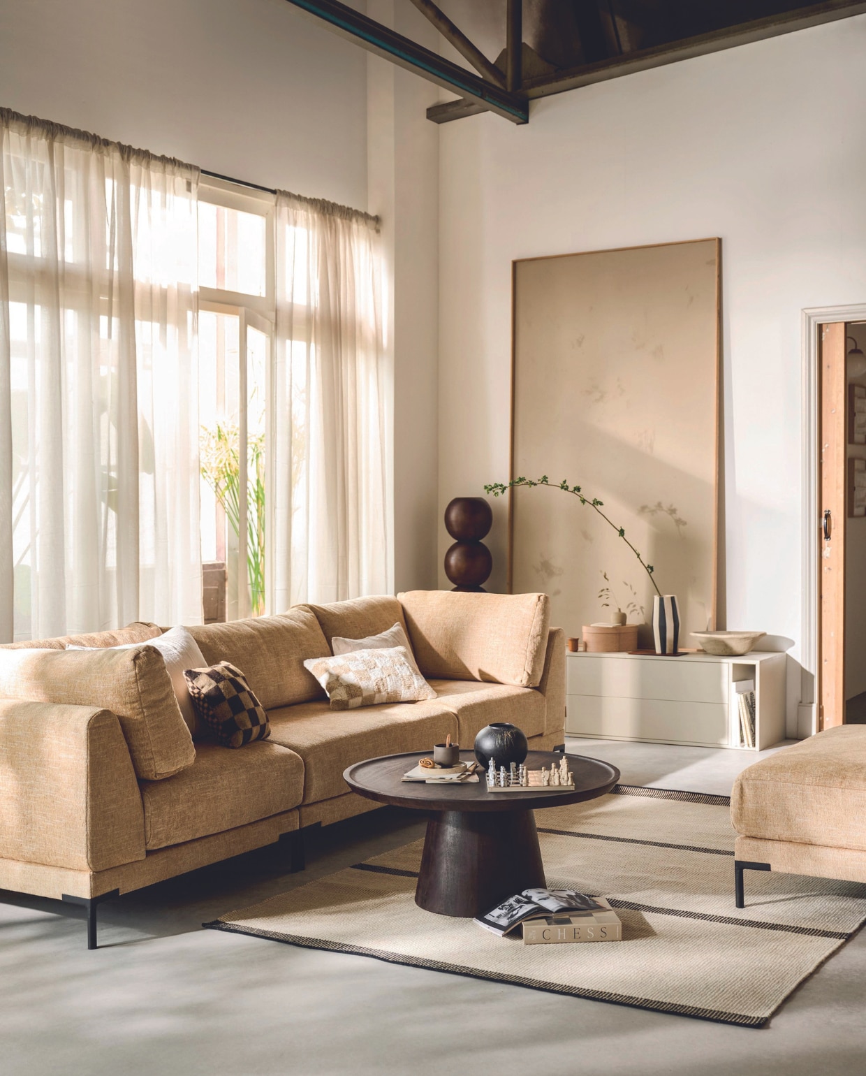 Elementenbank Couple in stof Butter Melange, zoals hier samengesteld: hoekelement links € 949,-, loveseat € 1049,- en hoekelement rechts € 949,-, verkrijgbaar in verschillende stoffen. Bijzettafel Coffee A Gogo, mangohout en walnootfineer, 90x40 cm (Øxh) € 499,-. Loveseat Couple in stof Butter Melange, 100x100x89 cm (lxbxh) € 1049,-, verkrijgbaar in verschillende stoffen. Grenenhouten tv-meubel Settle Down in Dust, 200x44x45 cm (bxdxh) € 499,-.M.m.v. vtwonen.nl/shop (vloerkleed van Linie Design), velv.nl (kussens Eve en Pure, mok, minivaas op tv-meubel), urbannatureculture.com (sokkel Bulb), zarahome.com (doos, schaal), hm.com (gordijnen), wehkamp.nl (kussen blokpatroon van Nous Living). Overig privébezit. vtwonen 07-2024 | styling Sanne Ketelaar | fotografie Sjoerd Eickmans