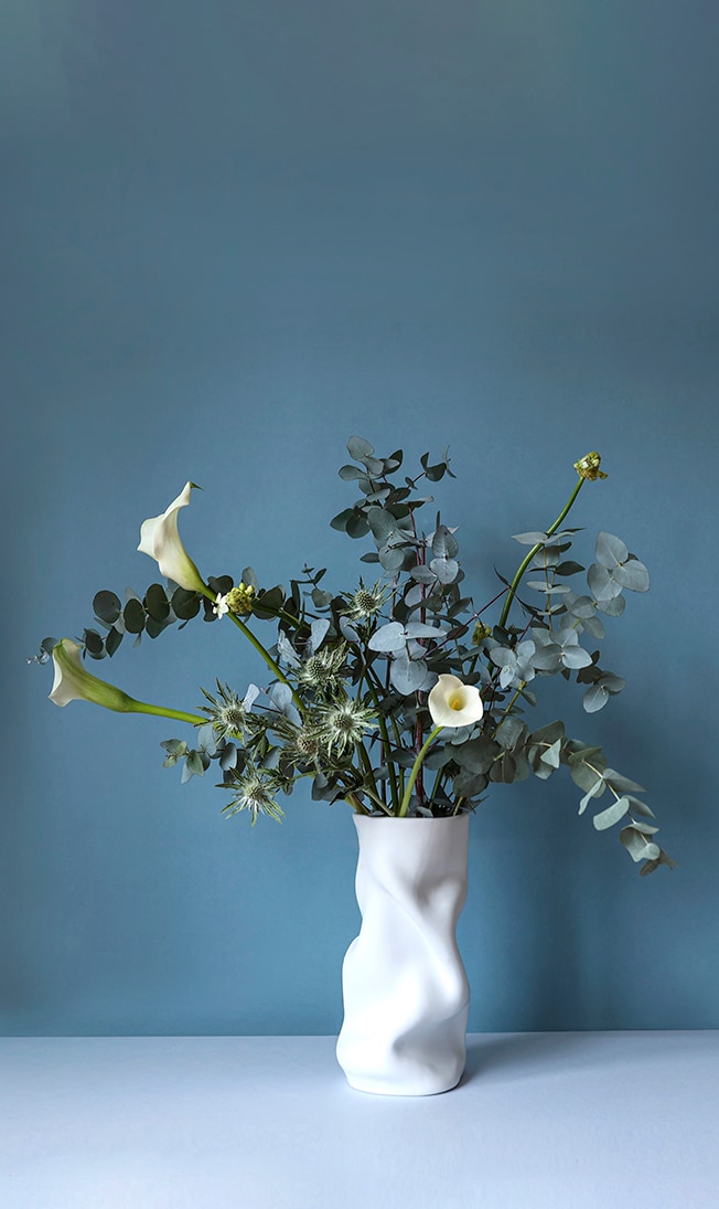 De organische vorm van vaas Collapse van Menu matcht goed met het weelderige groen: eucalyptus en distels aangevuld met enkele calla lelies. De scherpe distels vormen een interessant contrast met de zachte vormen van de vaas, terwijl de lelies net die gebogen lijnen herhalen. Distel, eucalyptus en calle lelies zijn het hele jaar door beschikbaar. Het is een handige combinatie waar je altijd naar kunt teruggrijpen. foto Kaatje Verschoren – met dank aan philippo-rozen.be voor de bloemen en gaest.design voor de vaas