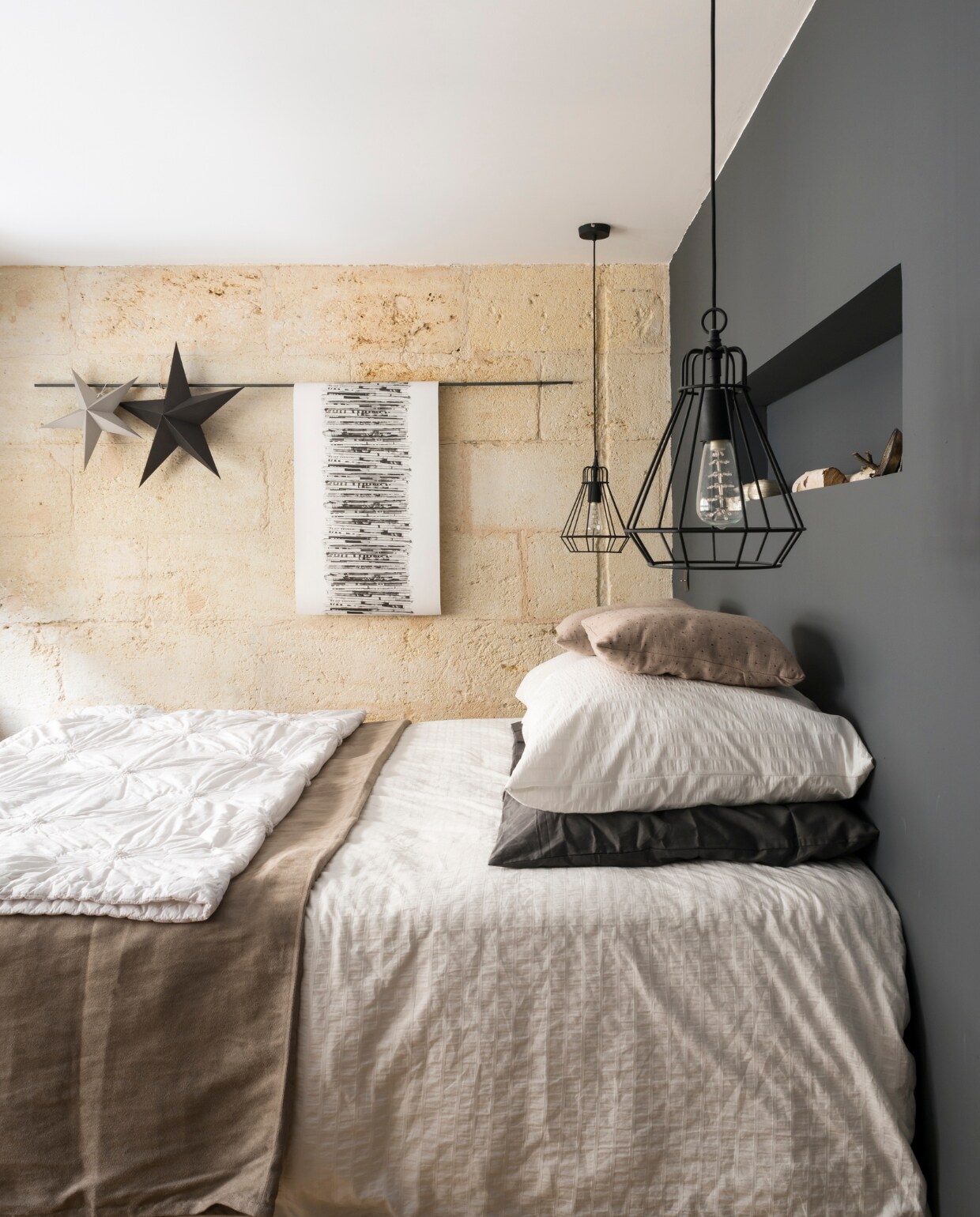 Eyecatcher in de ouderlijke slaapkamer is de originele stenen muur. De antracietkleurige wand biedt een eigentijds tegenwicht. Het bedlinnen is van Ikea, www.madurahome.com en Côté Table. De lampen zijn van Castorama, een Franse bouwmarkt. De print is een stuk behang. vtwonen 03-2015 | Fotografie Julien Fernandez / amandinejules.com