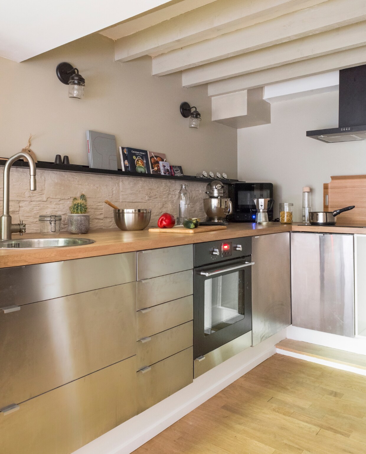 De keuken is van Ikea en werd uitgerust met een eikenhouten werkblad. Stenen panelen dienen als spatrand, afgezet met een donkere wandplank van Ikea. De wandlampen zijn gekocht op Etsy. Het trapje leidt naar de entree, langs een wand vol familiefoto’s, tekeningen en sierobjecten. Houten dienblad van Habitat, keukenmachine van Kitchen Aid. vtwonen 03-2015 | Fotografie Julien Fernandez / amandinejules.com