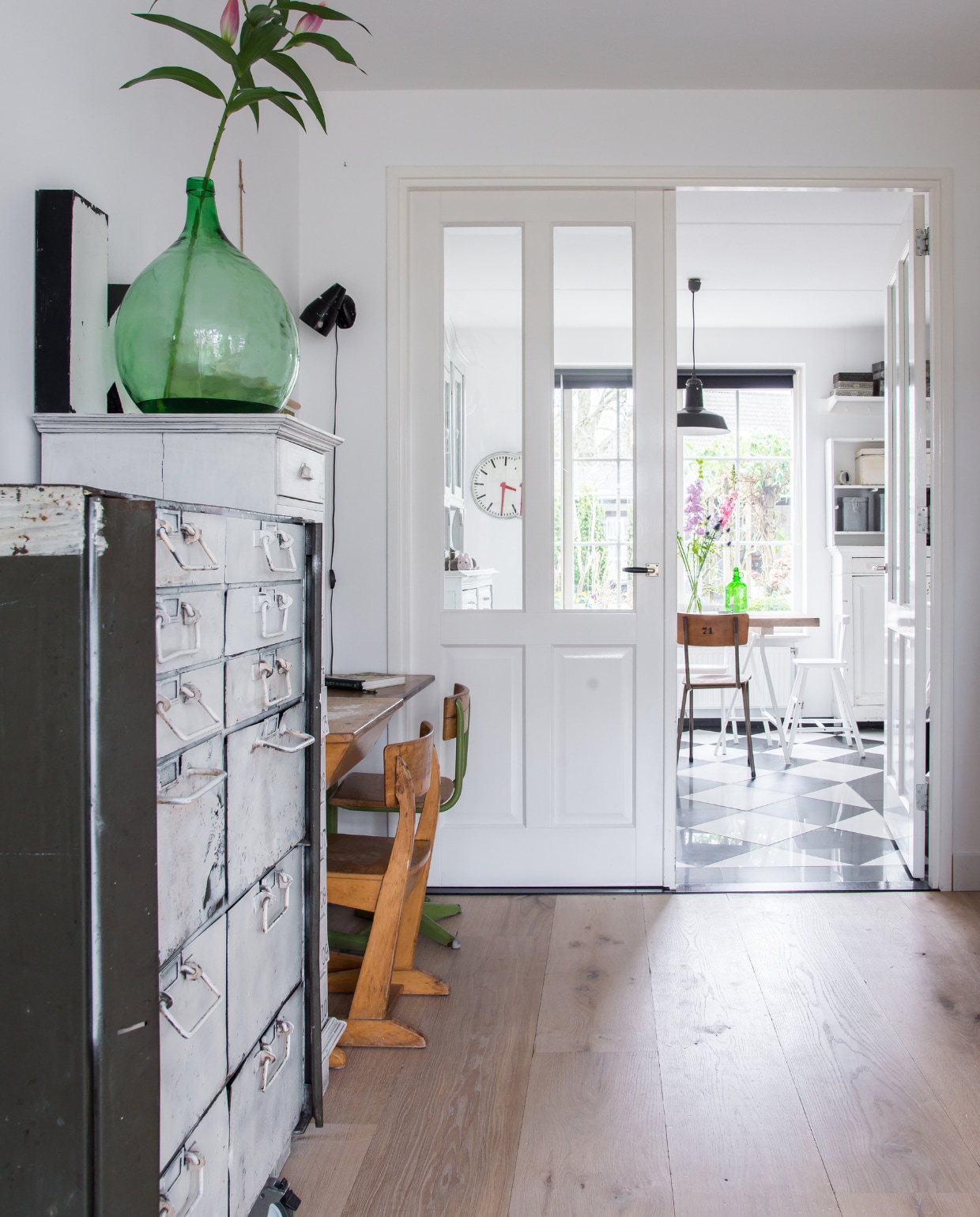 Keuken, lampen, planken, kruk en witte stoel Ikea. Tegels Karwei. Kinderstoel Ikea, stoelen Heavy Stuff. Vloer Tegeltoko, snoerlamp Juud &amp; Jul, kast en hanglamp van Marktplaats. De pendule van een rommelmarkt is wit geschilderd. vtwonen 12-2017 | styling José Spaans | fotografie Barbara Groen
