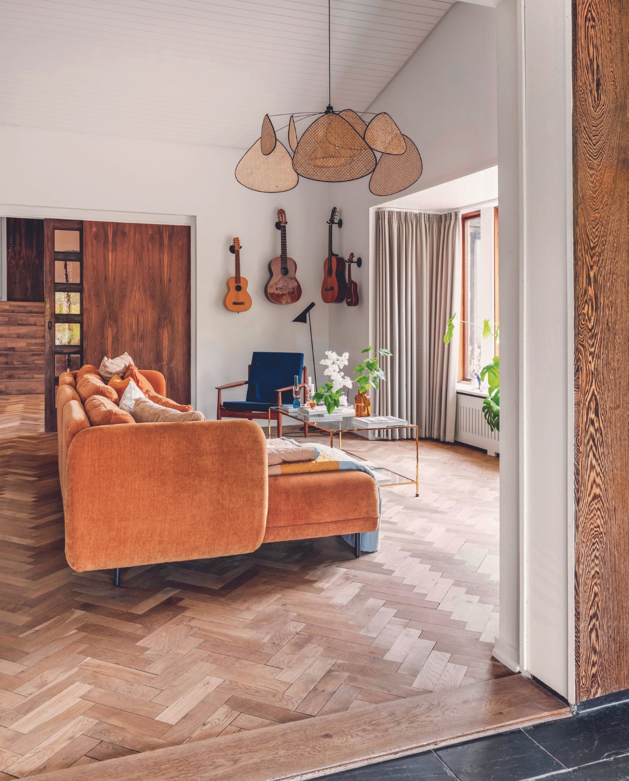 Stenen terras aangelegd door de vorige bewoners, tuintafel Fermob, stoelen Fdb Møbler, schapenvachten Ikea, tafelkleed Fabelab. De parketvloer is 75 jaar oud, bank Sofacompany, lamp Market Set, oude gitaren van Michaela, salontafel Ellos, kandelaars C’est Bon, vaas H&amp;M Home vtwonen 06-2024 | fotografie Christina Kayser Onsgaard | styling Rikke Graff Juel
