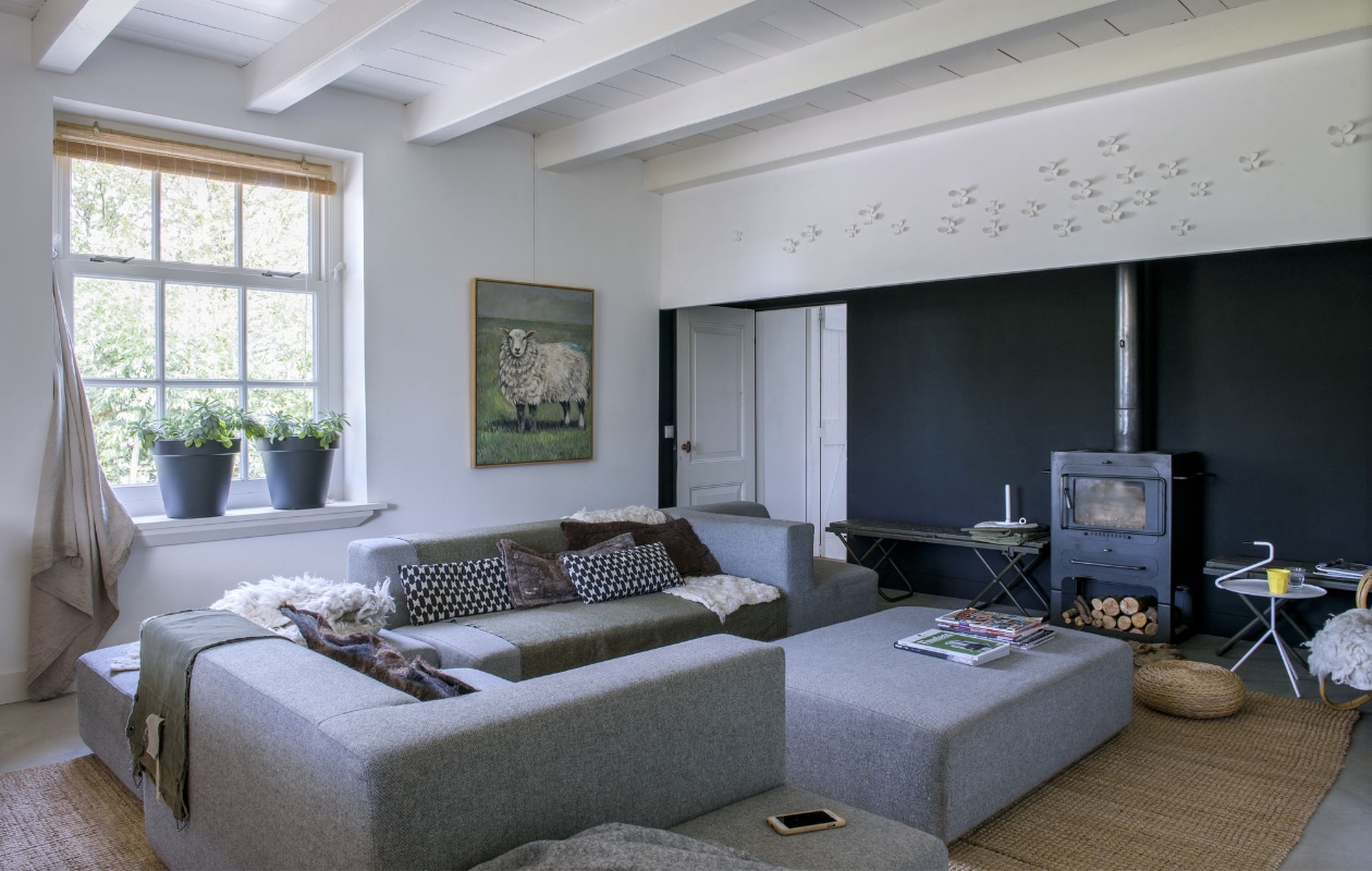 De woonkamer bevindt zich in de vroegere opkamer. De bank is van Sur + Plus, vloerkleed en zwart-wit kussen van Ikea, legerzak en plaid van Stapelgoed, plantenpotten van Karwei. De vilten kussens en kleden maakte Miranda zelf. Het schilderij is van Maja Philips. Op de wand witte bloemen van Umbra, als een knipoog naar ouderwetse wandbordjes. vtwonen 11-2019 | styling Monique van der Pauw | fotografie Ton Bouwer