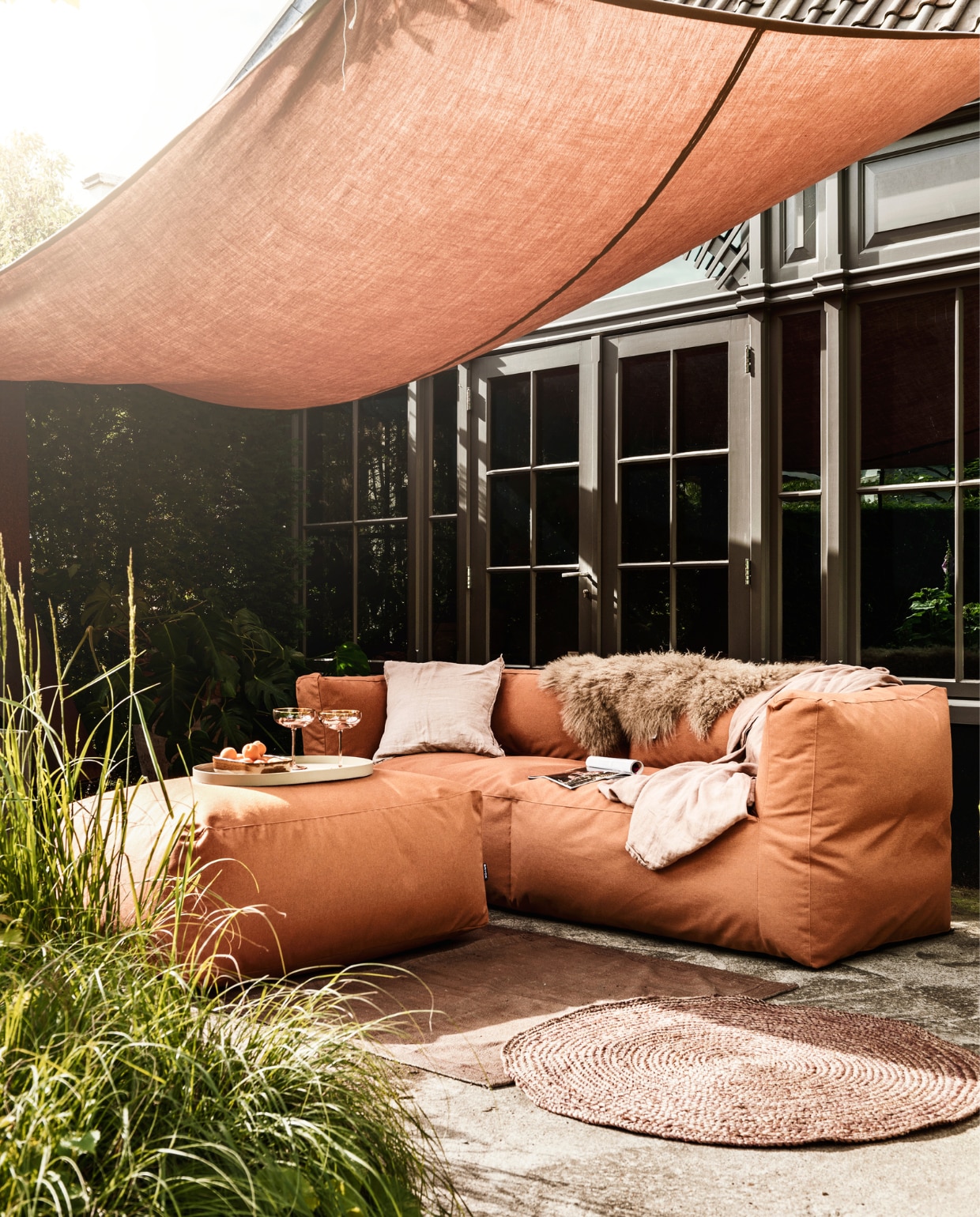 Zonnedoek gemaakt van zwaar linnen, Stone Washed Reloaded CH2559/066 van Chivasso, 139 cm breed per meter € 89,95 (jab.de). Driezits buitenmeubel, afmeting 223 x 80 x 76 cm € 1100,-, hocker € 375,-, rechthoekig vloerkleed € 150,- (brechtmurreatelier.nl). Rond gevlochten kleed, 1 m Ø € 100,80 (vtwonen.nl). Op de bank: Tibetaanse schapenvacht € 144,- (iblaursen.dk), linnen doek € 150,- (weldaad.nl), kussen met linnen hoes € 40,- (brechtmurreatelier.nl). Op de hocker: zandkleurig ovaal dienblad € 61,-, bord van Serax € 12,25 (vtwonen.nl), champagneglas per set van zes € 82,95 (nordal.dk). vtwonen 08-2019 | styling Marianne Luning | fotografie Stan Koolen