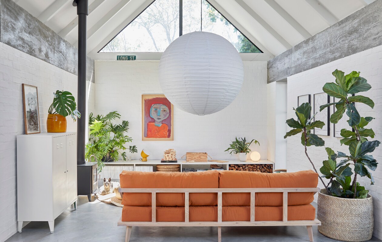 Maatwerk bank Kipekee Studio, stof in Tobacco van House of Fabrics (Kaapstad). Dressoir zelfgemaakt door Casey, ontwerp Beatty Vermeiren. Schilderij Jan Vermeiren, tafellamp Ikea PS collectie. Kachel Morsø, kast Mother City Hardware, gele plantenpot Pezula, muurverf Dulux. Vergelijkbaar: rijstpapieren hanglamp Hay, mand Urban Nature Culture. Planten onder andere Monstera en Ficus lyrata. vtwonen 07-2024 | productie Frank Features / Living Inside | fotografie Greg Cox