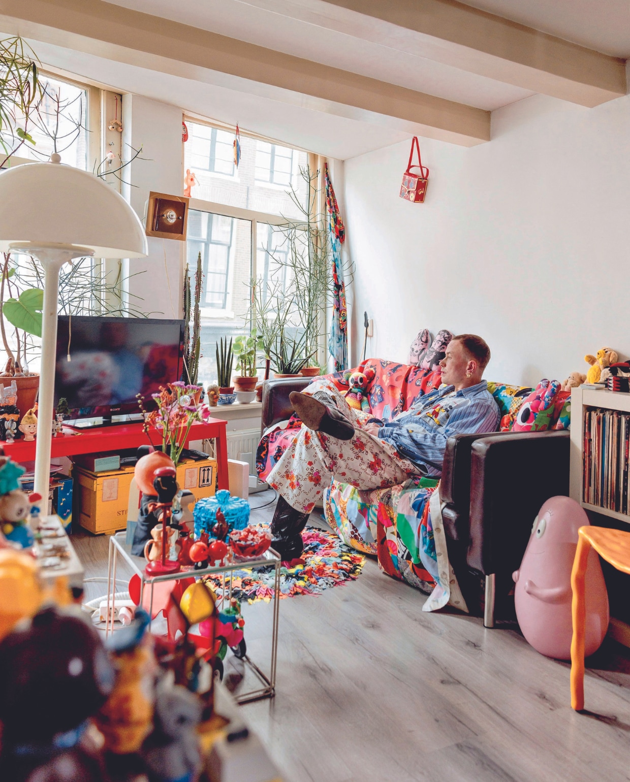 Bas’ bank ligt bomvol poppen en kussens. Hij past er zelf nog nét op. Bijzettafel Nesting van Max Sauze, wandlamp Raak, gele legerkist vintage. Ook vintage is de quilt die Bas op een vlooienmarkt in het Rose Bowl Stadion in Los Angeles vond. vtwonen 08-2024 | fotografie Ernie Enkelaar