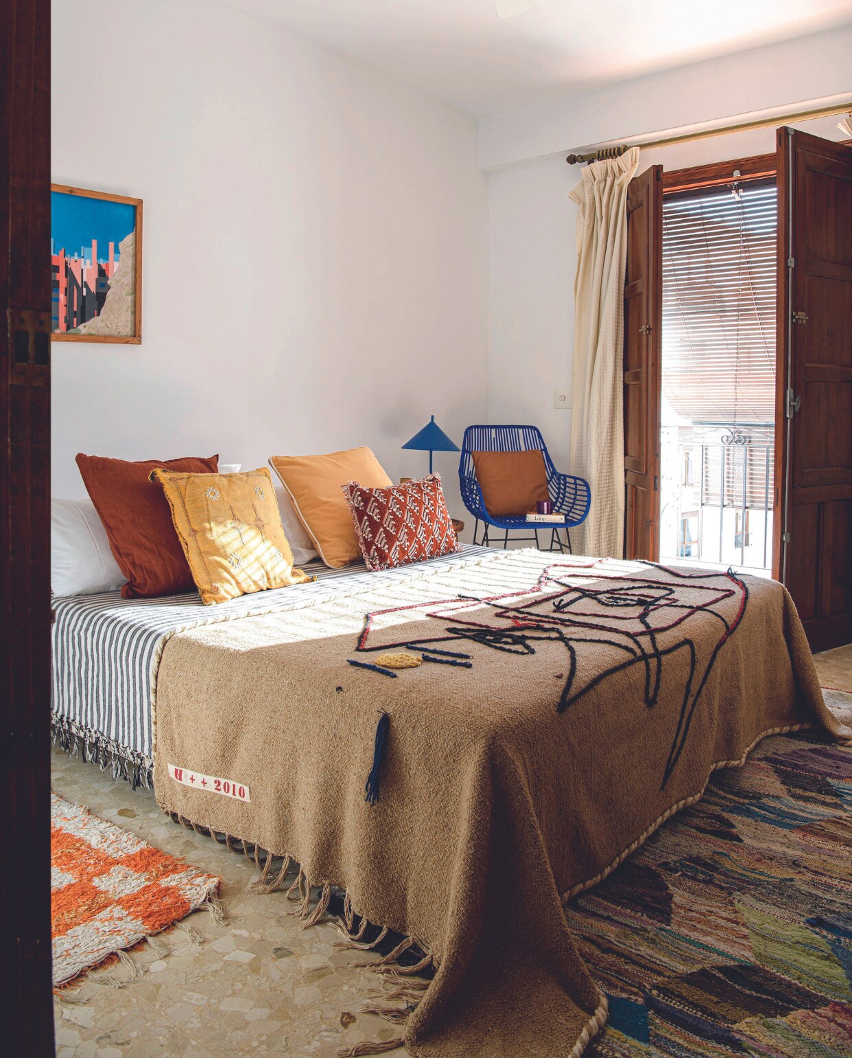 Schilderij gemaakt door opa, oranje geblokt vloerkleed uit Bisbal, meerkleurig vloerkleed herkomst onbekend, bruine sprei Honoré via Esprit de Sel, Carcassonne, zwart-witte sprei Zara Home, kussens Madam Stoltz, brocante en Maisons du Monde, stoel tweedehands, lamp Jessica Bataille, gordijn Borja Home. vtwonen binnenkijkspecial 07-2024 | productie Insidehomepage | styling Esther Loonstijn | fotografie Louis Lemaire