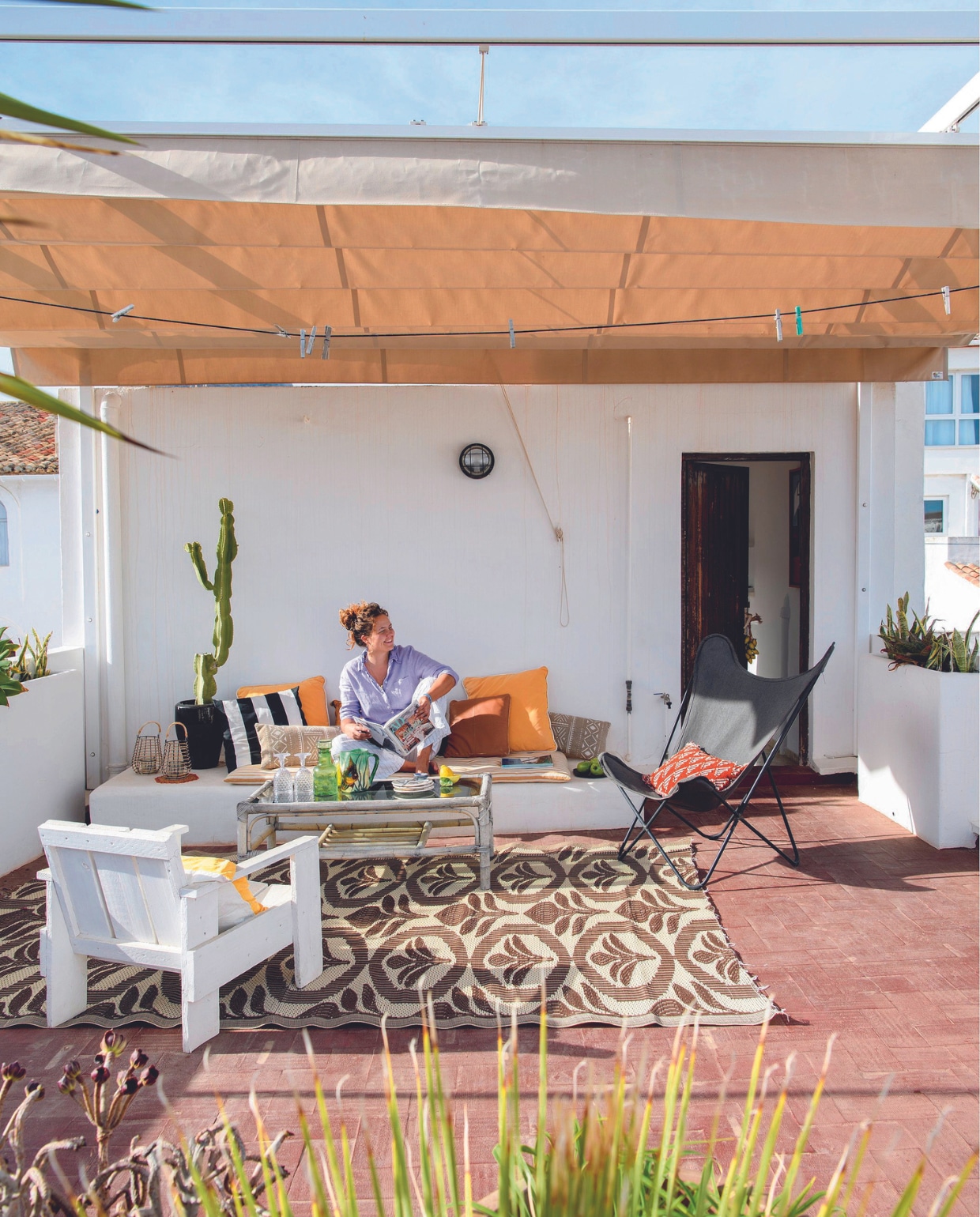 Buitenkleden uit Marokko, zwarte vlinderstoel familiestuk opnieuw bekleed, zwart-wit gestreept kussen Madam Stoltz, leren kussen Tine K Home, overige kussens Maisons du Monde, Borja Home, brocante en gemaakt door oma, witte stoel gemaakt door vader, tafel en citroenkom La Luciole, kaarshouders Borja Home, kunststof wijnglazen Guzzini, groene stopfles antiekmarkt in Frankrijk, inbouwbank en plantenbakken gemaakt door lokale timmerman. vtwonen binnenkijkspecial 07-2024 | productie Insidehomepage | styling Esther Loonstijn | fotografie Louis Lemaire