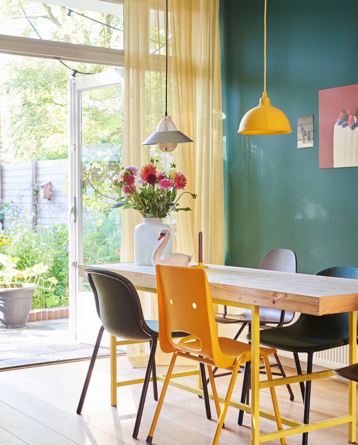 Tafel zelfgemaakt. Herkomst gele lamp onbekend. Linker lamp van Klaas Kuiken Donkere kuipstoelen: de Vorm, houten stoel Spoinq, gele stoel Erik Stehmann. Gordijnen Kvadrat, print met taart van Saakje, print met paard Tryntsje Nauta. Muurkleur: Mid Azure Green van Little Greene via Drent &amp; Van Dijk. vtwonen 06-2019 | fotografie Ronald Zijlstra