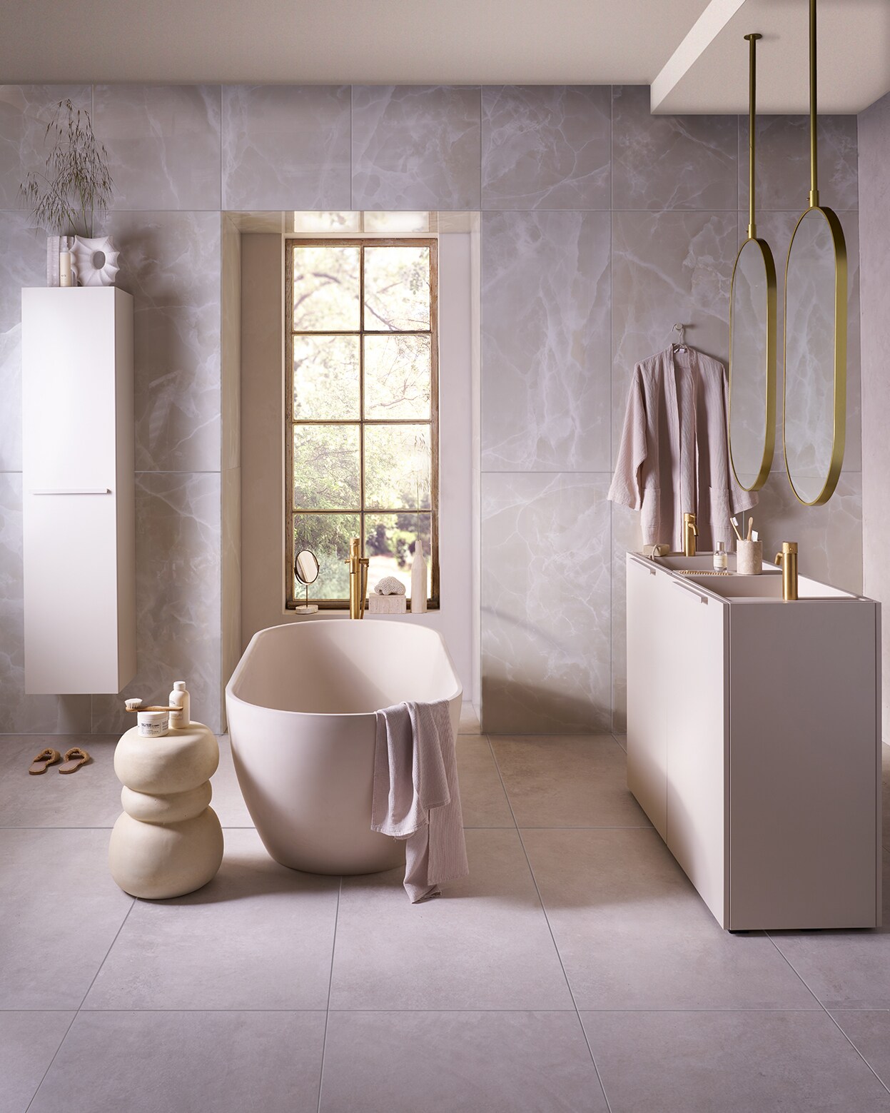 Op de vloer tegels Noble White, 60x120 cm, per m² € 69,50. Op de wand tegels Onyx Crystal White, 60x120 cm, per m² € 92,50. Top Solid bad Endless in zand, 160x73x57 cm (lxbxh), inhoud 200 liter € 4175,-. Kunststof kolomkast Bend met handgreep in matzand, 40x35,5x172 cm (bxdxh) € 1729,-. Spiegels Oval in goud, 60x90 cm (bxh) € 550,-, ook verkrijgbaar in andere afmetingen. Kunststof onderkast Wide in matzand, met twee openslaande deuren, 124,6x44,4x90 cm (bxdxh) € 1300,-, Top Solid wastafel Wide in matzand, 121x40,5x20 cm (bxdxh) € 1095,-, Top Solid plateau voor wastafel in zand, 36,8x15x8 cm (bxdxh) € 208,-. M.m.v. plieger.nl (kranen Roma, badkraan Roma), vtwonen.nl/shop (kruk van Woood), zarahome.com (badlaken, kimono, slippers, beker, zeep, borstel, spiegel op voet, travertin box), hm.com (vaas met gat), urbannatureculture.com (vaas met ribbels), lelabofragrances.com (shampoo, bodycrème, parfum). vtwonen 09-2024 | Fotografie Jeroen van der Spek | Styling Cleo Scheulderman
