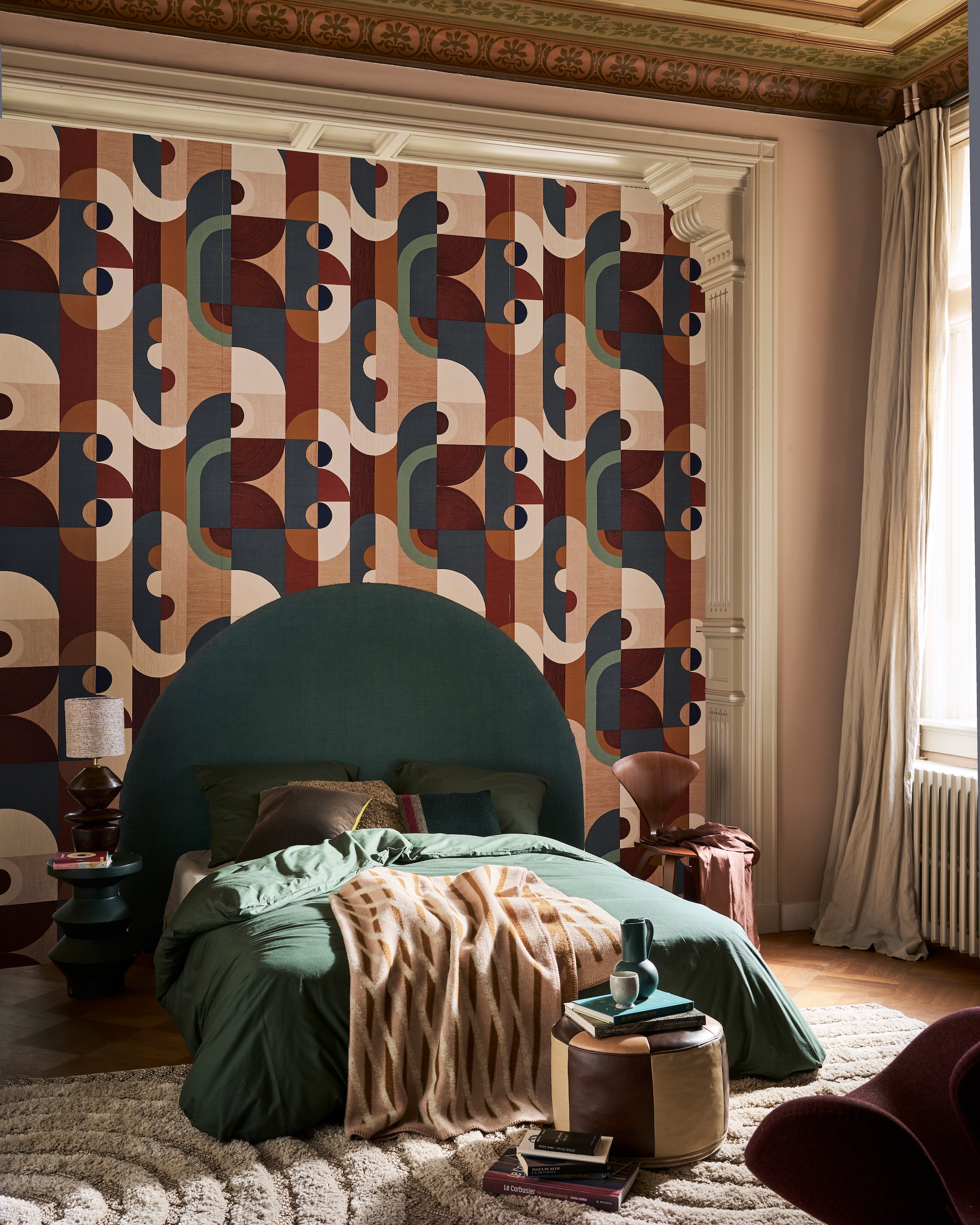 Muurverf Setting Plaster 231 van Farrow &amp; Ball (vestingh.nl). Behang Vassily uit de Mouvement-collectie nr. 75990610, 70 cm x 10 m (bxl), per rol € 148,50 (casamance.com). Hoofdeinde op maat (stoffeershop.nl), met stof Linara in kleur Bonsai van Romo Fabrics, 140 cm breed € 66,50 (romo.com). Katoenen dekbedovertrek, 220x240 cm € 34,99 (hm.com). Wollen deken van Roros Tweed, 135x200 cm € 229,- (debijenkorf.nl). Vintage Norman Cherner eetkamerstoel € 600,-, vintage fauteuil Swan van Arne Jacobsen in bordeauxrood € 1850,- (@iconic_objects). Vintage vloerkleed, 195x290 cm € 875,- (bestwelhip.nl), leren poef € 85,- (redesignvintage.nl). Groene bijzettafel Rook, 48 cm (h) € 254,- (versmissen.nl). Tafellamp Venue van BePureHome, 50 cm (h) € 139,-, zwart-groen kussen van HKLiving € 36,99, kussen Birgit van by Fonq  € 26,35 (vtwonen.nl). Petrolblauwe kan van Raawii € 75,- (groenenakker.nl).  Overig privébezit. vtwonen 11-2024 | fotografie Jeroen van der Spek | styling Cleo Scheulderman