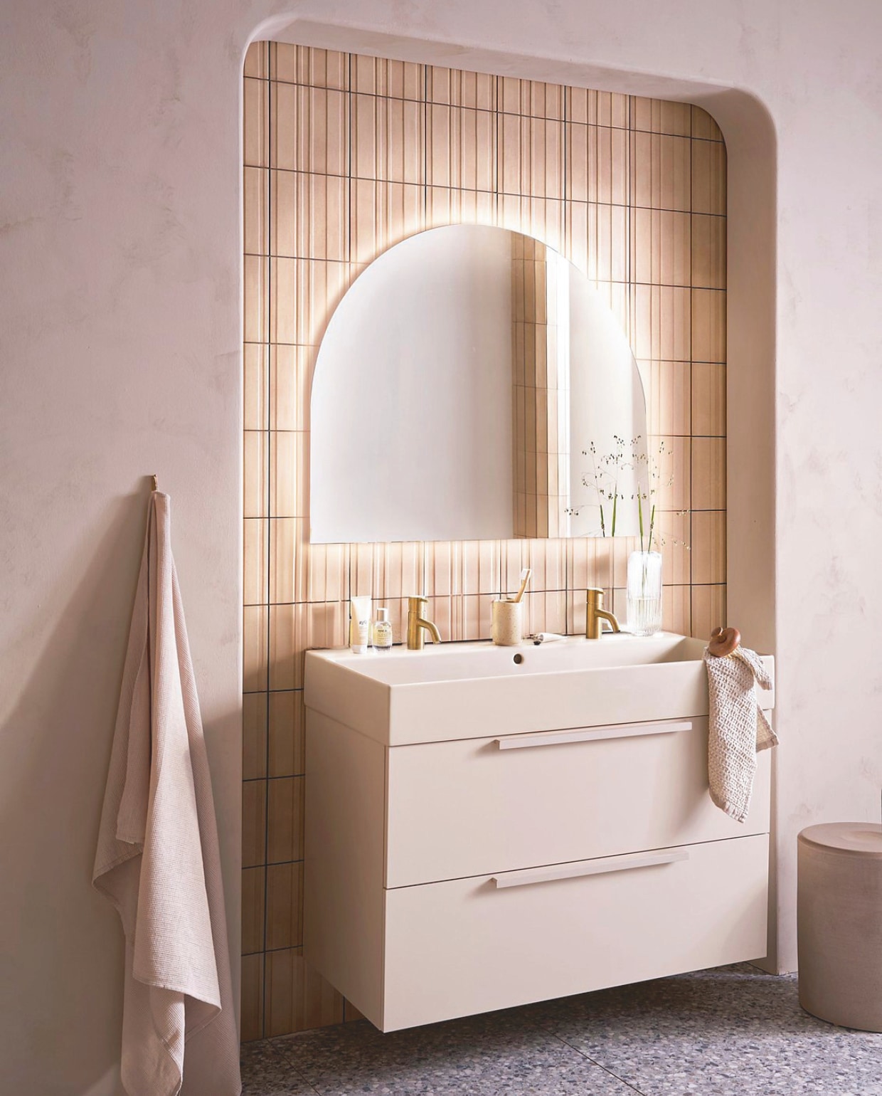 Op de wand tegels Earth Calce 3D Decor, 20x20 cm, per m² € 64,50. Op de vloer tegels Terrazzo Smoke Flakes, 60x120 cm, per m² € 74,50. Spiegel Design, half rond met indirecte verlichting, 100x80 cm € 998,-, ook verkrijgbaar zonder verlichting en in andere afmetingen. Kunststof onderkast Tidy in matzand, twee lades met handgreep, 120x40,5x40 cm (bxdxh) € 1362,-, Top Solid wastafel Wide in zand, twee kraangaten, 120x41x20 cm (bxdxh) € 1095,-. M.m.v. plieger.nl (kranen Roma in geborsteld goud), vtwonen.nl/shop (kruk van Serax), zarahome.com (badlaken, beker, zeep, kimono), lelabofragrances.com (parfum). Overig privébezit. vtwonen 09-2024 | styling Cleo Scheulderman | fotografie Jeroen van der Spek