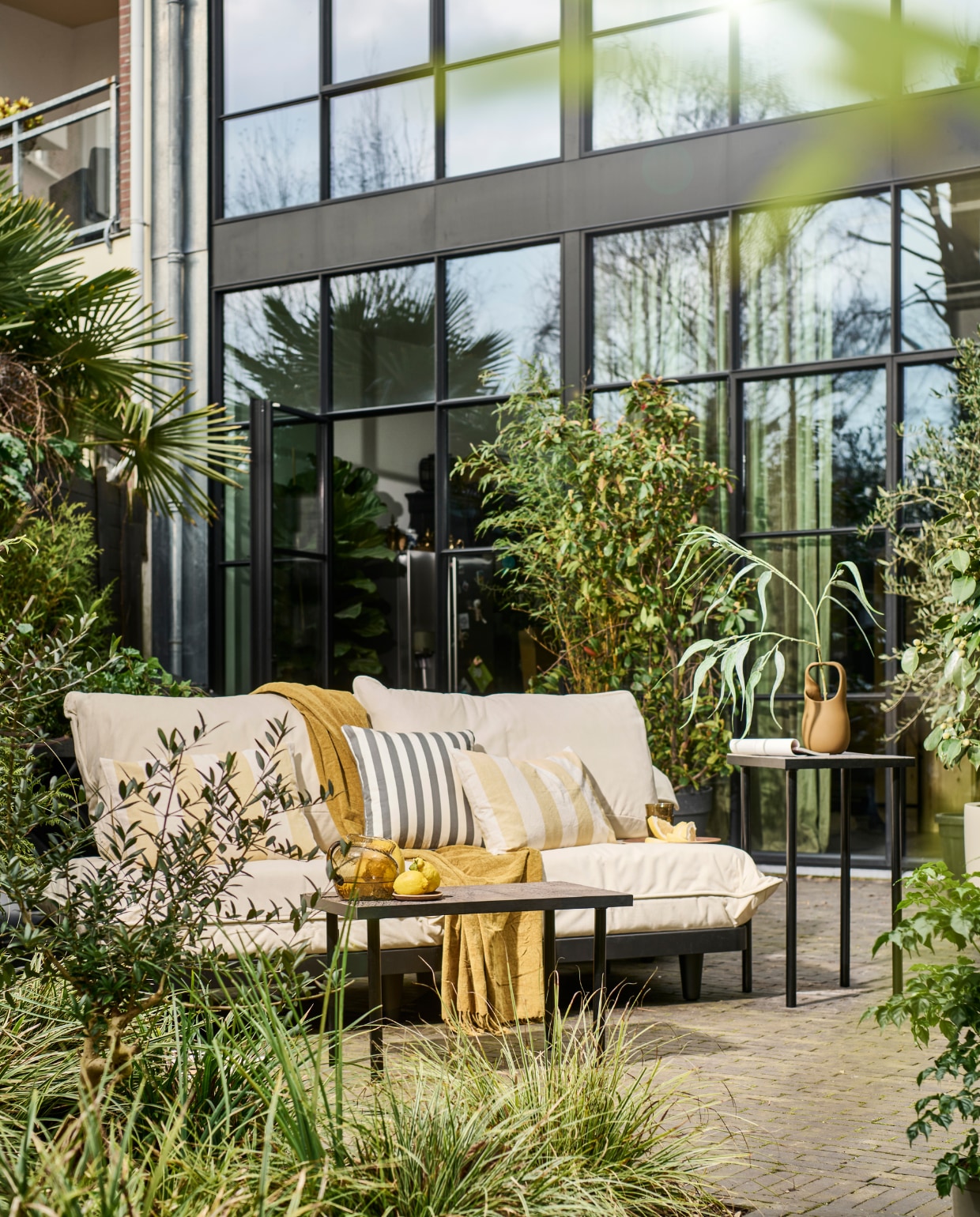 Modulaire loungeset Paletti van Fatboy, kunststof frame met waterafstotende kussens € 899,-, bruine stenen vaas Nicita van Bloomingville € 58,90 (vtwonen.nl/shop). Plaid € 12,99, blauw gestreept kussen € 17,99, geel gestreept kussen € 17,99, glazen karaf € 29,99, houten onderzetter € 5,99, houten dienblad € 17,99, drinkglazen € 5,99 (zarahome.com). Overig privébezit. vtwonen 08-2023 | styling en uitvoering Sanne Ketelaar | fotografie Sjoerd Eickmans