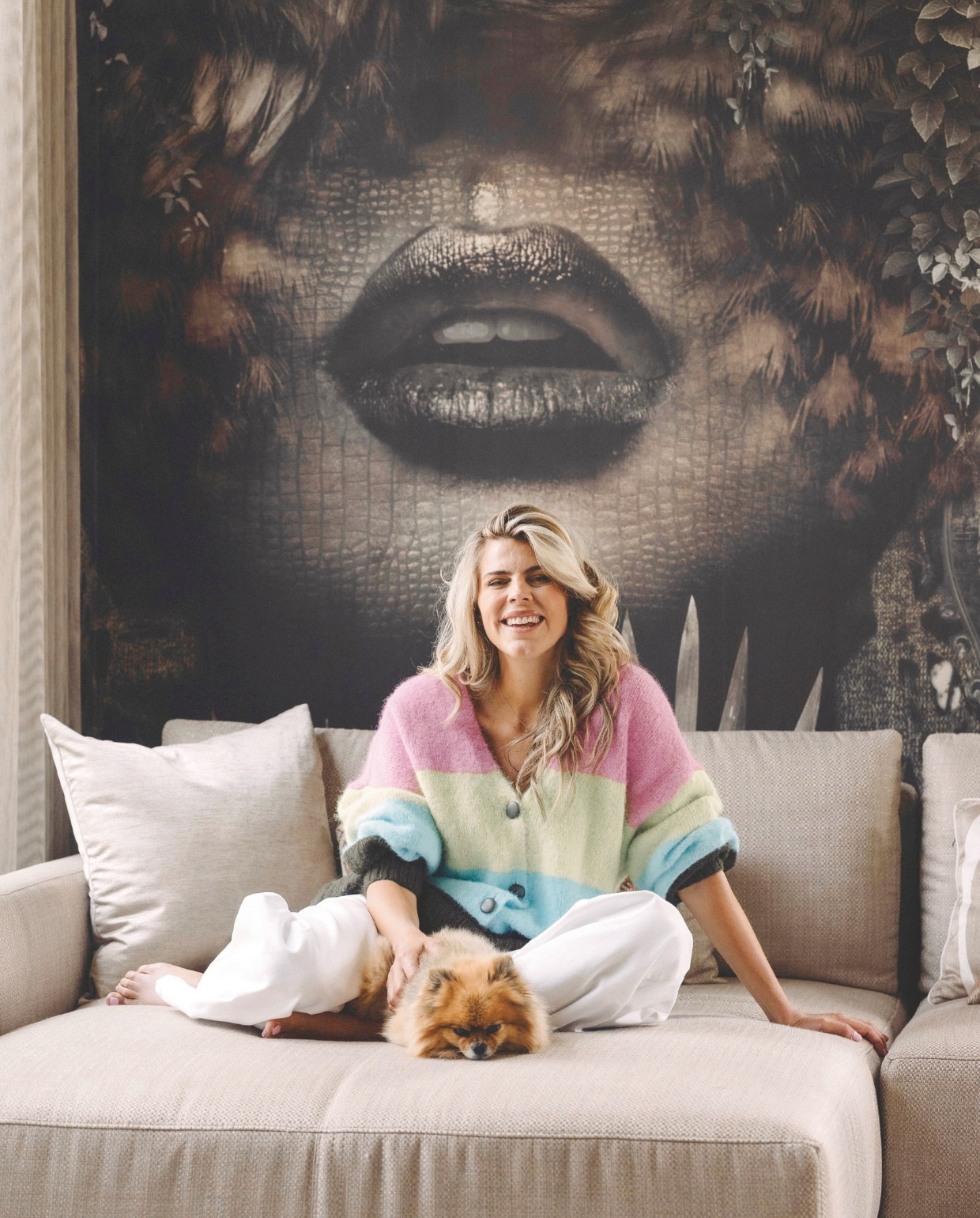 Kim met hondje Snoet op de bank van Passe Partout via Kötter Living. Het behang heeft Poespas-ontwerper Dennis gemaakt. stijlvol wonen 9-2024 | Fotografie Stefanie De Neve
