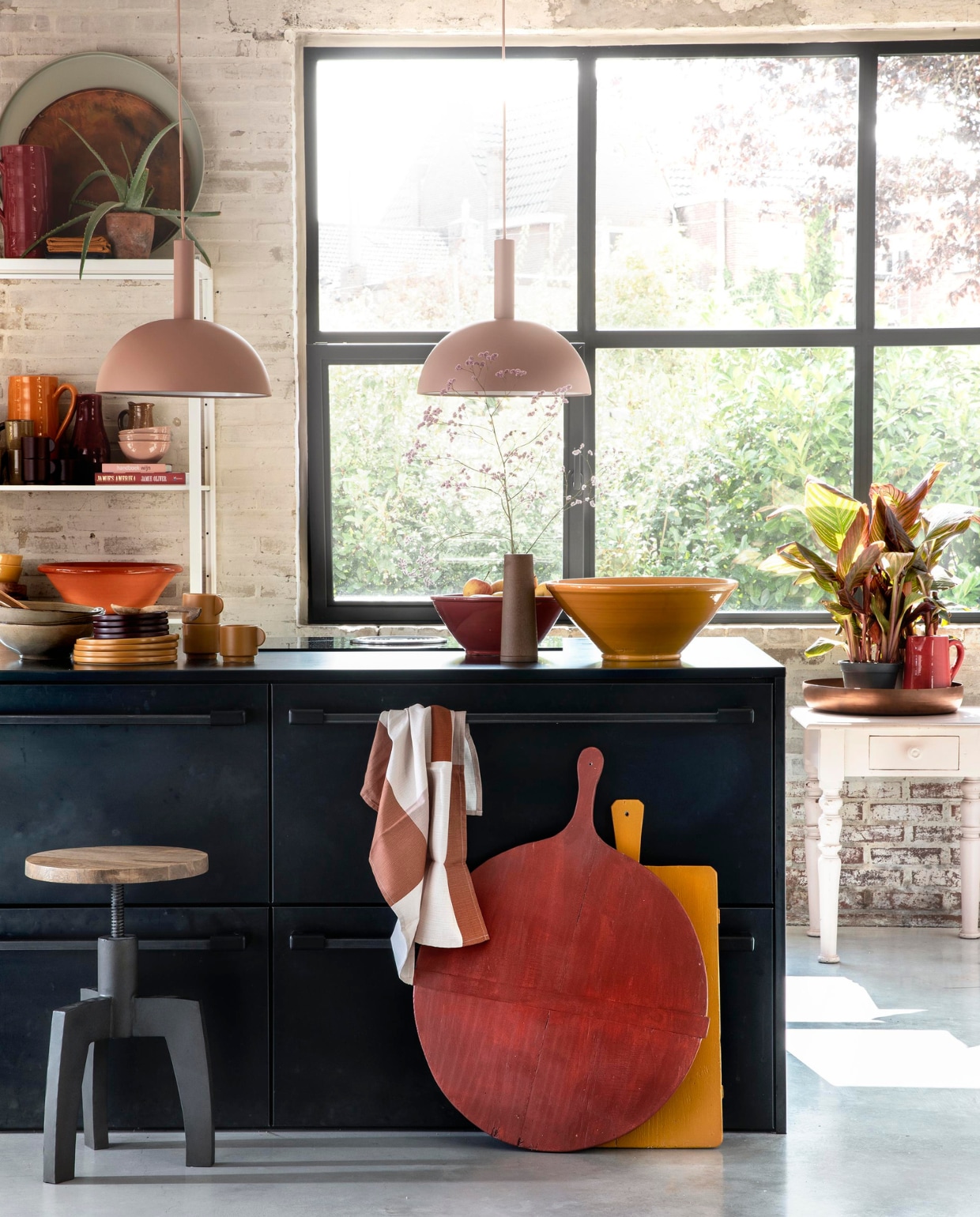 Zachtroze hanglampen Dome Shade van Ferm Living inclusief roze fitting high per stuk € 269,- (vtwonen.nl). Draaikruk Space van BepureHome € 99,- (Woondock). Grote oude kaasplanken per stuk € 35,- (H&amp;M Home), gelakt met Perfection zijdeglans lak in dieprood en mosterdgeel, 750 ml € 25,99 (Histor). Theedoek € 4,99, okergele kopjes per stuk € 5,99, okergele borden per stuk € 7,99, donkerpaarse borden per stuk € 4,99 (H&amp;M Home). Okergele schaal € 35,-, donkerrode schaal € 25,- (In-Petto). Beige schalen per stuk € 12,49 (Intratuin). Bovenop de kast: grote donkerrode kan € 35,- (In-Petto), theedoeken in okergeel en donkerpaars per stuk € 4,99 (H&amp;M Home), koperkleurige schaal van BePureHome € 39,95, zachtgroene schaal € 24,95 (Woondock). Midden in de kast: zachtroze schaaltjes per stuk € 7,50, okergele kan € 35,- (In-Petto). Donkerpaarse kopjes per stuk € 5,99 (H&amp;M Home). Donkerrode karaf Nikki € 21,99, lichtbruine karaf € 8,99 (Intratuin). Beige kan € 8,99 (Intratuin). Onder in de kast: terracotta schaal € 35,-, okergele diepe borden € 12,50 (In-petto). Zachtroze tafeltje € 175,- (Combitex). Koperkleurige schaal Big Waitress van BePureHome € 24,95 (Woondock). Donkerrode kleine kan € 25,- (In-Petto). Kamerplanten Canna Hybride per stuk € 9,99 (Intratuin). De keuken is een eigen ontwerp van de bewoners, binnenwerk van hout, blad en kasten afgewerkt met blauw staal. Overig privébezit. vtwonen 11-2018 | styling Moniek Visser | fotografie Peggy Janssen