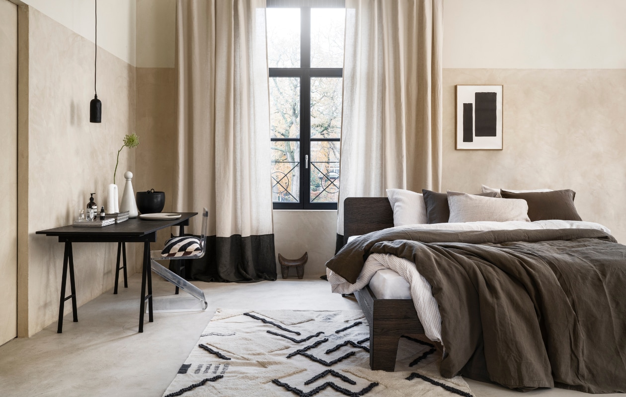 Stucco-look muurverf Mykonos, 2,5 liter € 110,- (wearewowmakers.com). Gordijn gemaakt van linnen Cloud Rider van Chivasso, per meter € 114,50 (jab.de). Bedombouw Pure, eiken fineer in Charcoal olie, 180x200 cm (bxd) € 3400,- (Loof). Duurzaam gewassen linnen dekbed-overtrekset met smalle strepen, 240x220 cm € 329,- (yumeko.be). Bruine dekbedovertrekset, duurzaam linnen en katoen, 240x220 cm € 179,95 (suite702.com). Vloerkleed, 260x160 cm € 399,- (malagoon.com). Tafel van Serax, 150x75x73cm (lxbxh) € 824,-, vaas met bolvormig deksel van Ferm Living € 85,-, schaal Omhu van Ferm Living € 105,- (flinders.be). Vintage transparante zigzagstoel € 350,- (Neef Louis). Hanglamp € 79,95, pot met oor € 62,95 (urbannatureculture.com). Vaas met twee poten van vtwonen € 49,95, gestreept kussen van Oyoy € 54,99 (vtwonen.be). Poster met lijst vanaf € 95,- (loods5.com). Afrikaans krukje privébezit. vtwonen 03-2023 | styling Marianne Luning | fotografie Stan Koolen